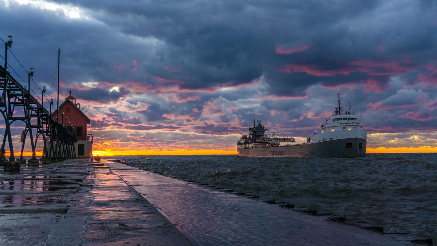 dramatic sunset over harbor with large cargo ship and pier under stormy clouds.