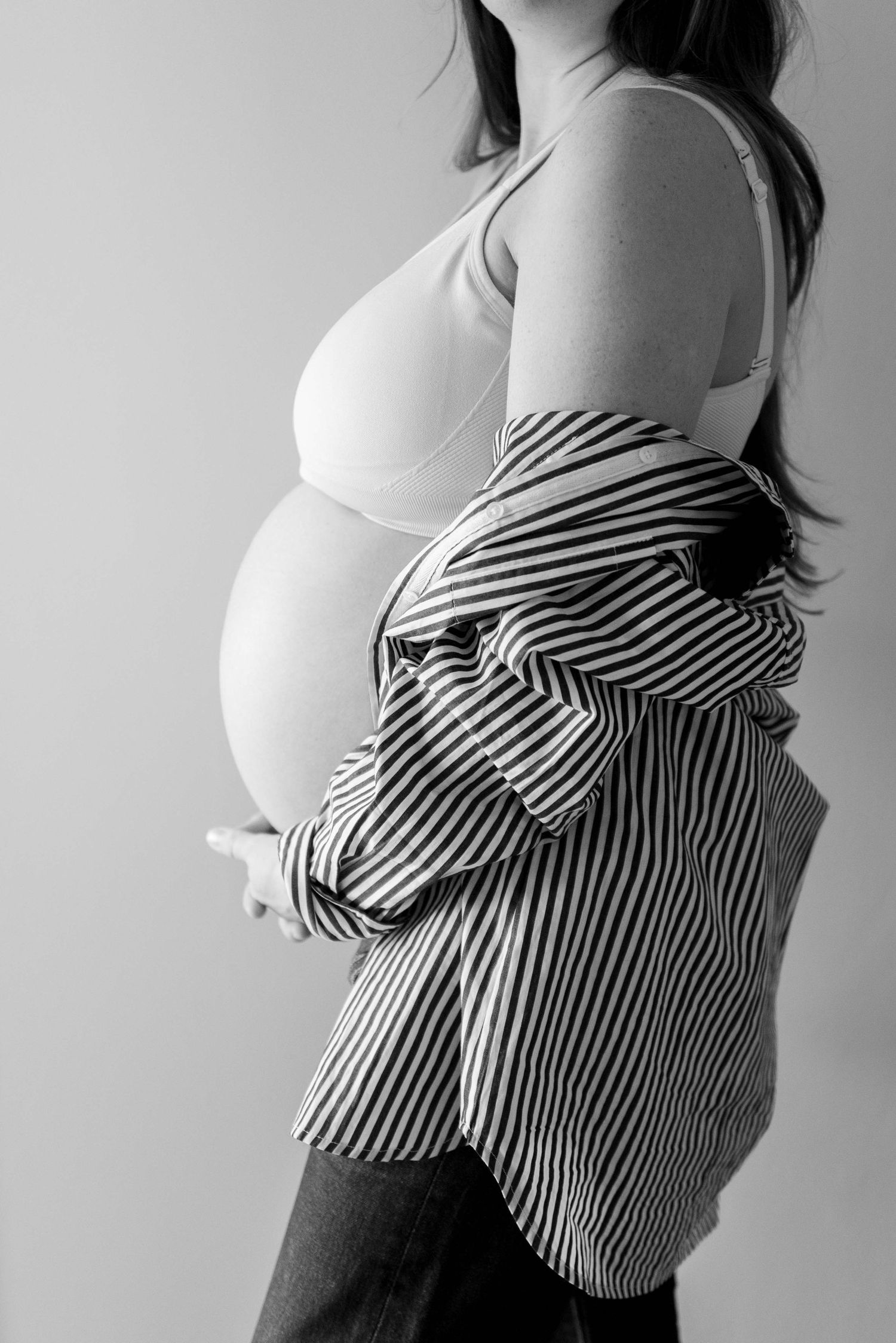 Black and white photo of pregnant woman in striped shirt and bra cradling baby bump.