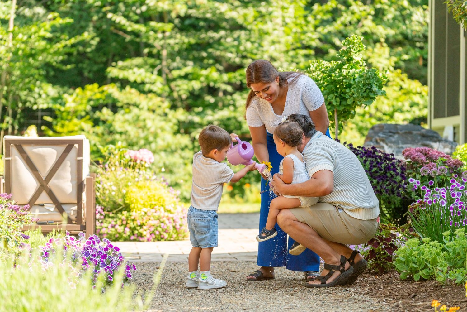 Family with two young children enjoying a lush garden path surrounded by colorful flowers and greenery.