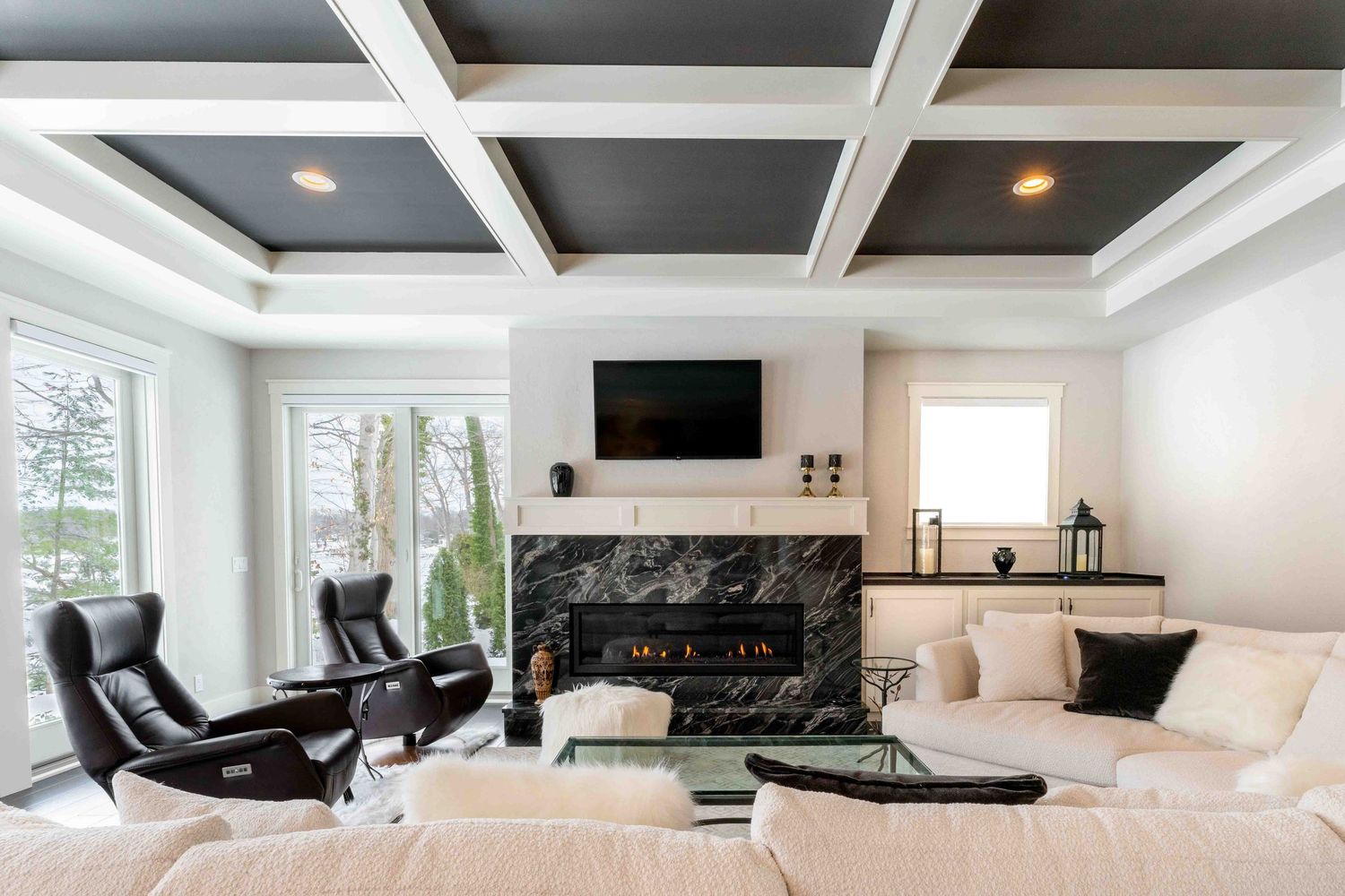 Elegant living room with black coffered ceiling, marble fireplace, and white sectional sofa.