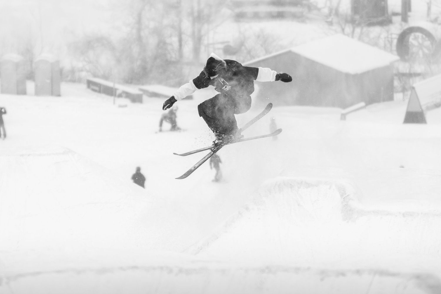 Skier launches off a snow jump in a blizzard at a winter terrain park.