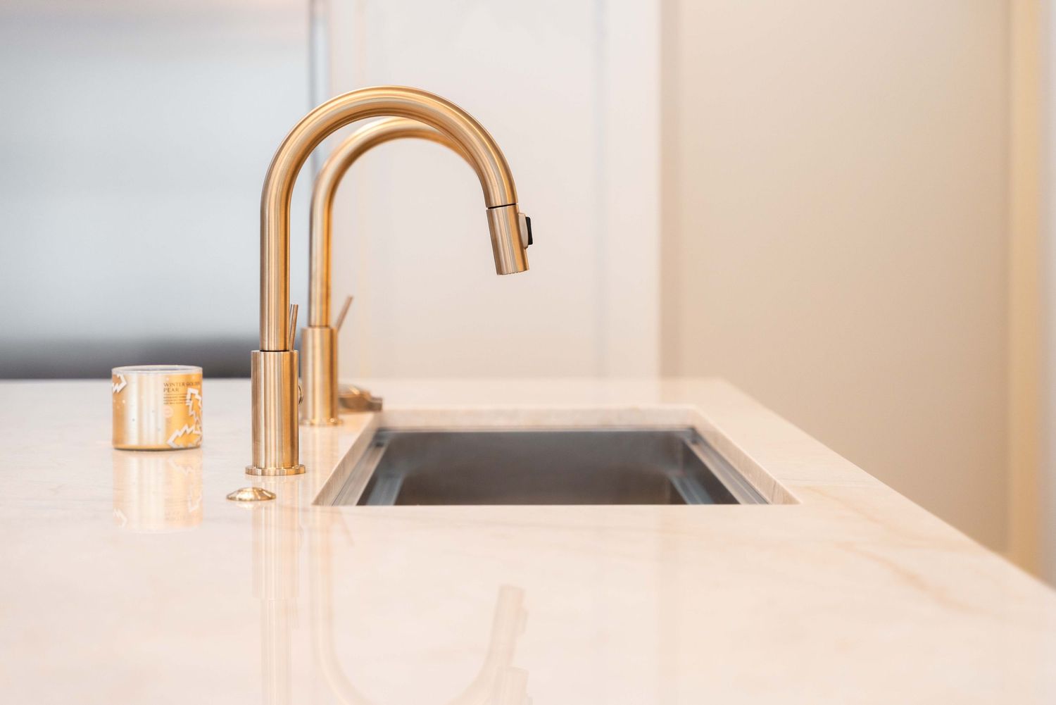 Gold gooseneck faucet over undermount sink on white marble kitchen countertop.