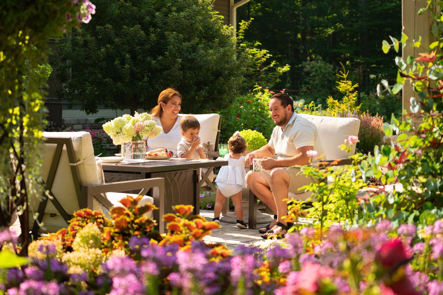 Family enjoying outdoor dining surrounded by colorful blooming flowers in a garden.