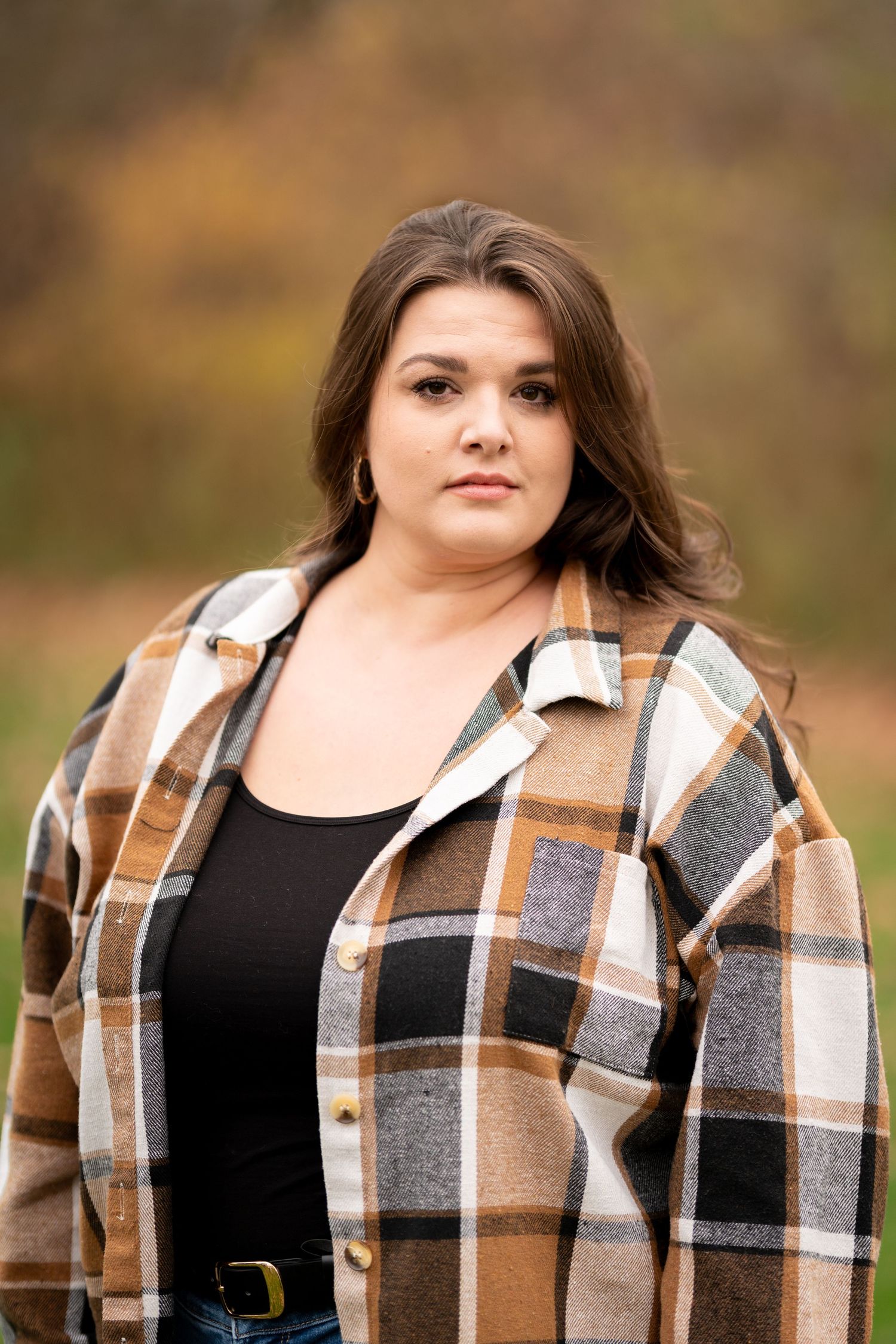 Young woman in plaid flannel shirt posing outdoors in autumn setting.