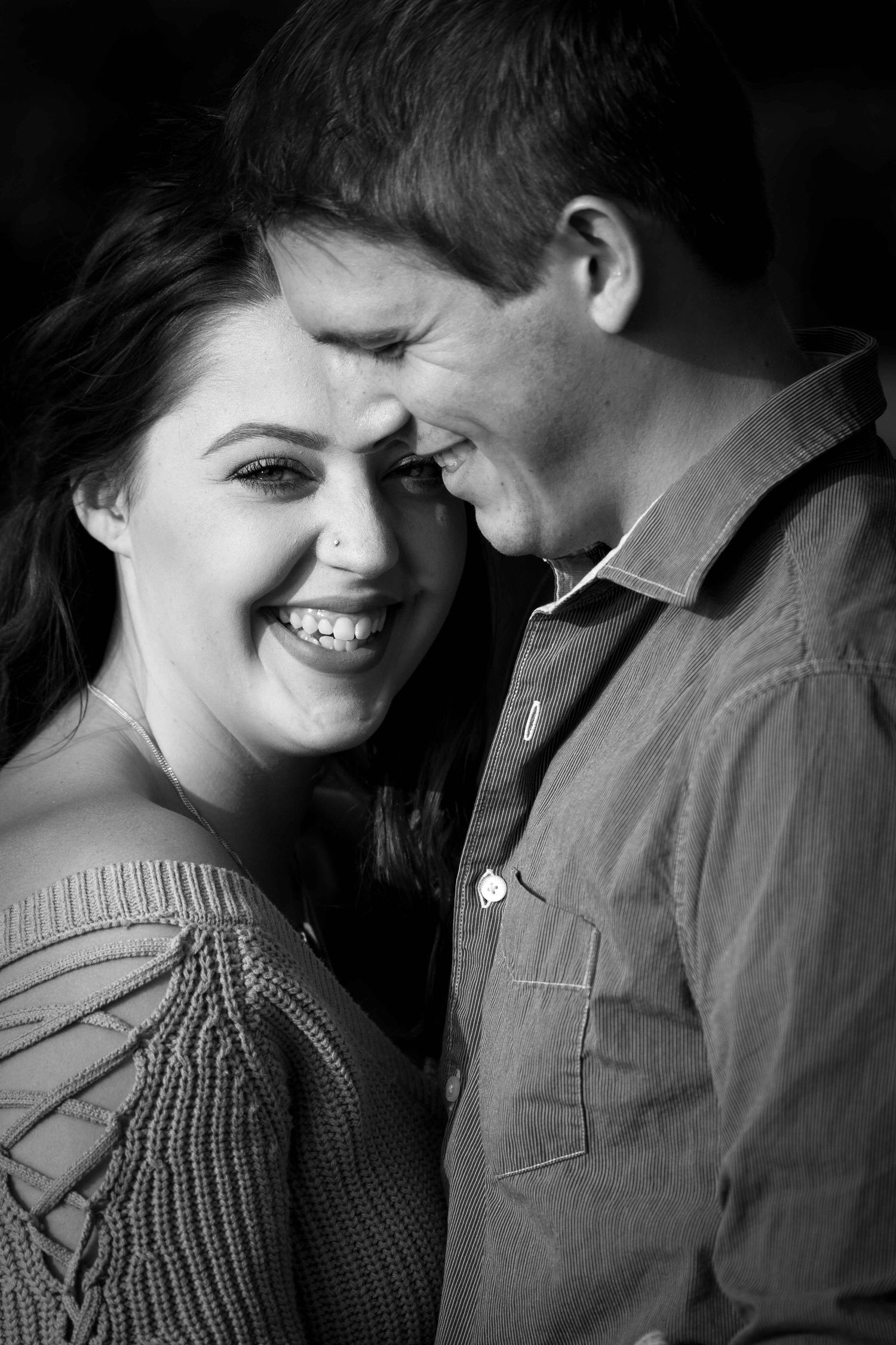 A joyful couple laughing together in an intimate black and white portrait.