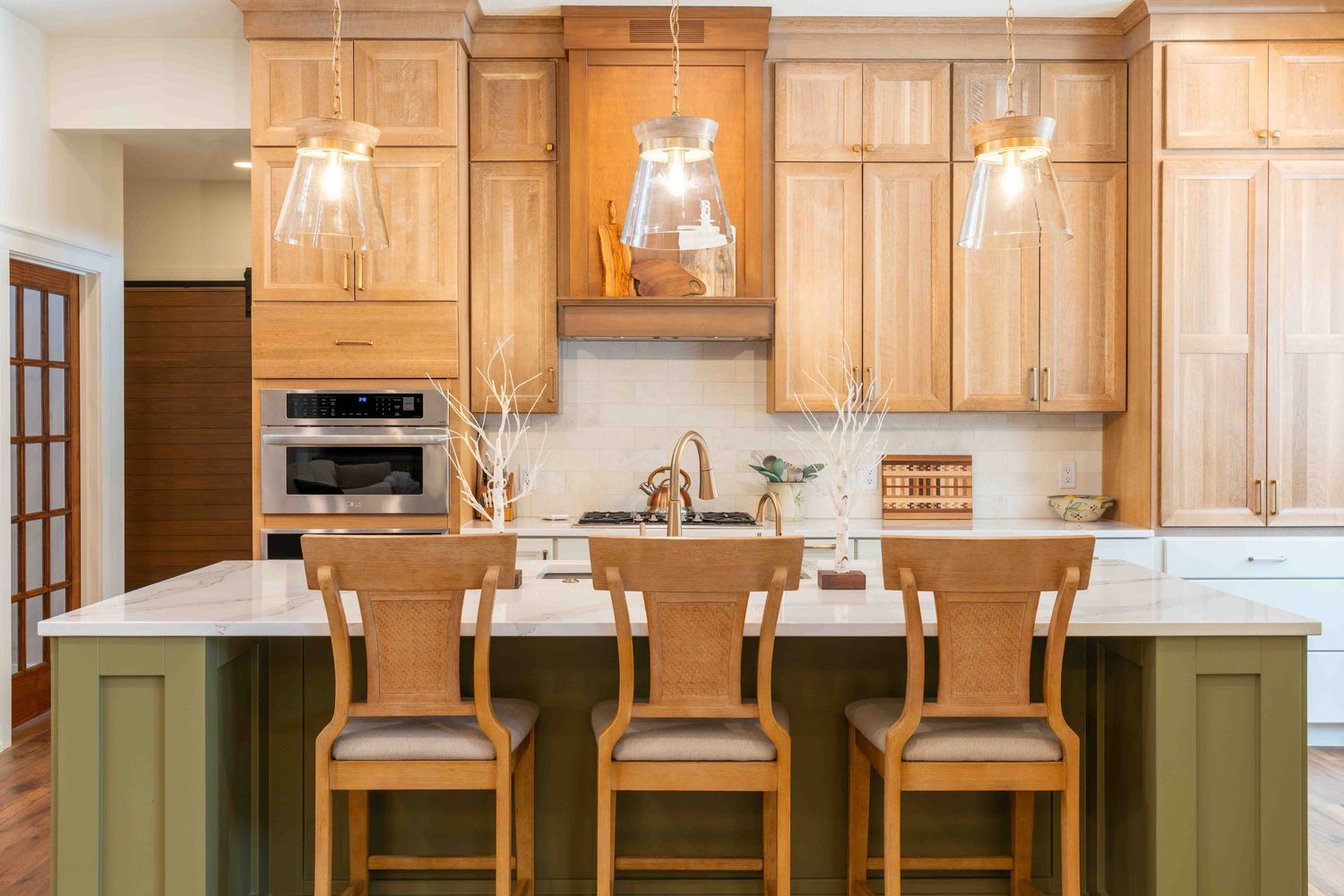 Bright kitchen with natural wood cabinets, green island, bar stools, and glass pendant lights.