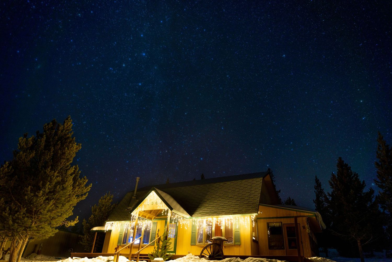 Cozy illuminated cabin glowing warmly under a stunning starry night sky in a snowy winter landscape.