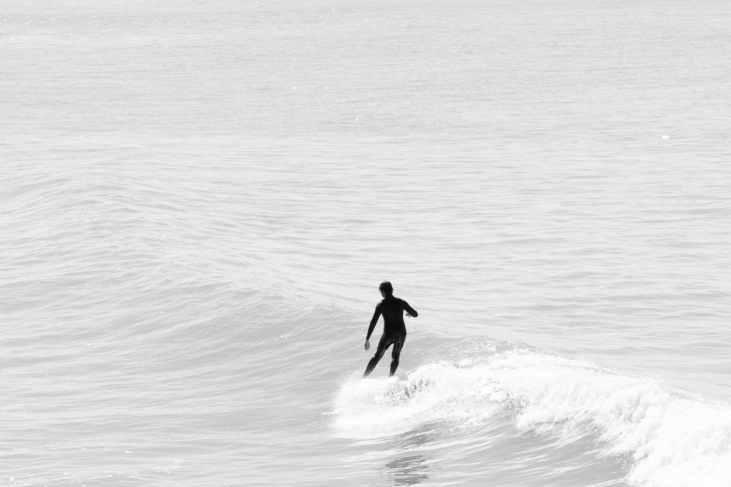 Black and white silhouette of surfer riding ocean wave in minimalist seascape photograph.