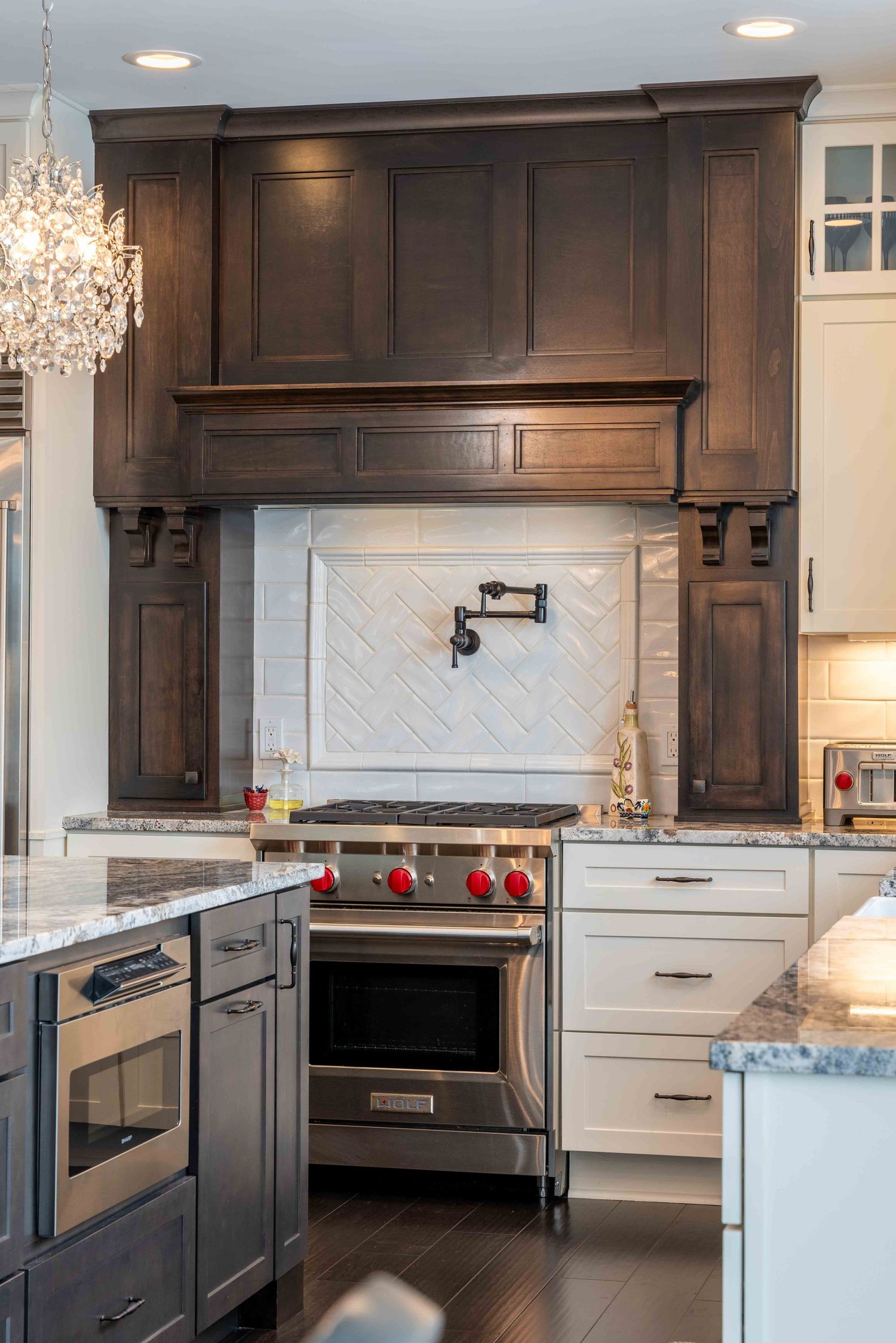 Luxury kitchen with dark wood range hood, herringbone backsplash, and stainless steel stove.
