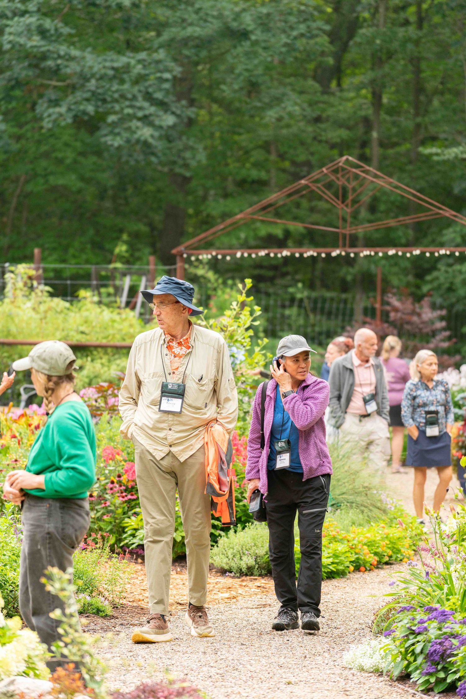 Visitors strolling through a vibrant summer garden event with colorful flowers and lush green trees.