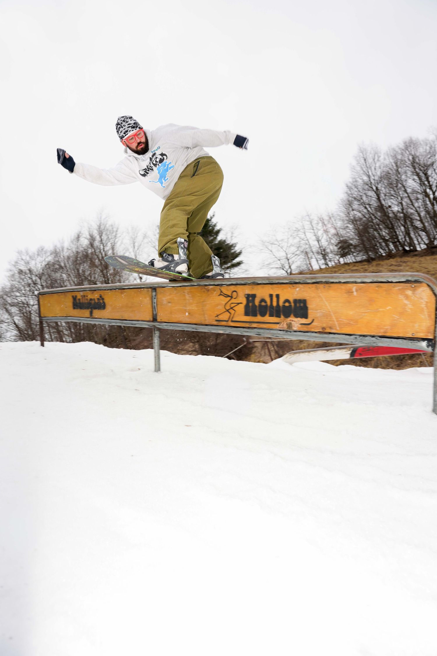 Snowboarder performing a rail grind trick at Holligan Hollow terrain park in snowy winter conditions.