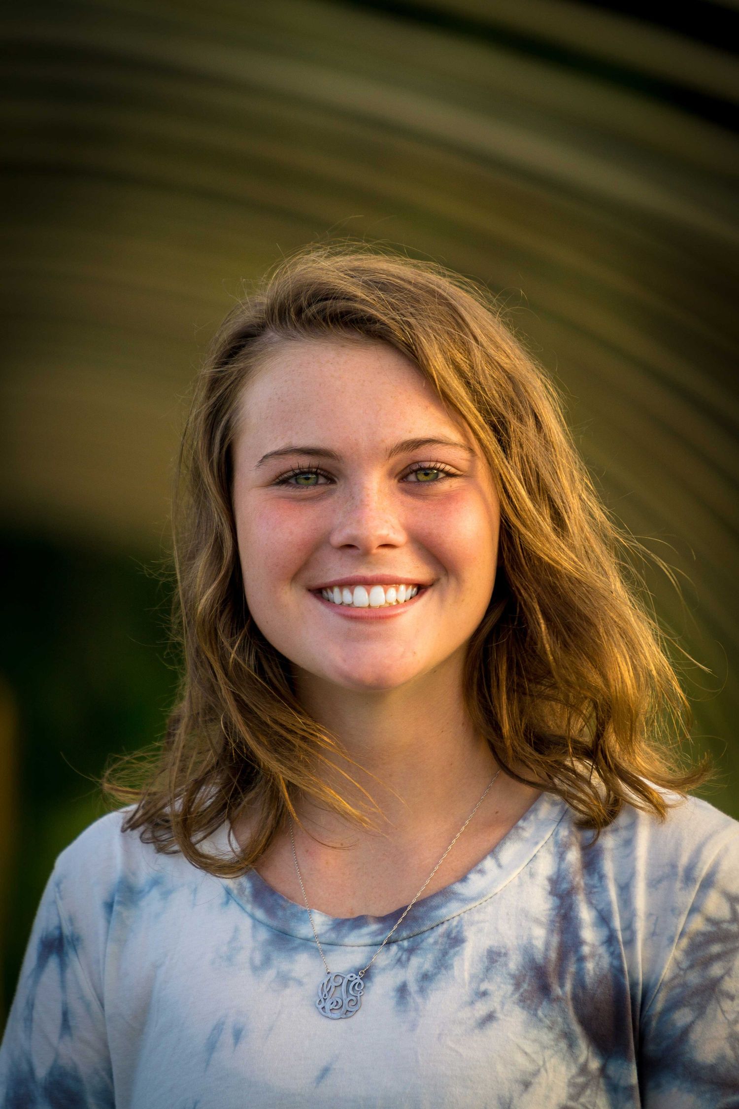 A smiling teenage girl with blonde hair wearing a tie-dye shirt in warm golden light.