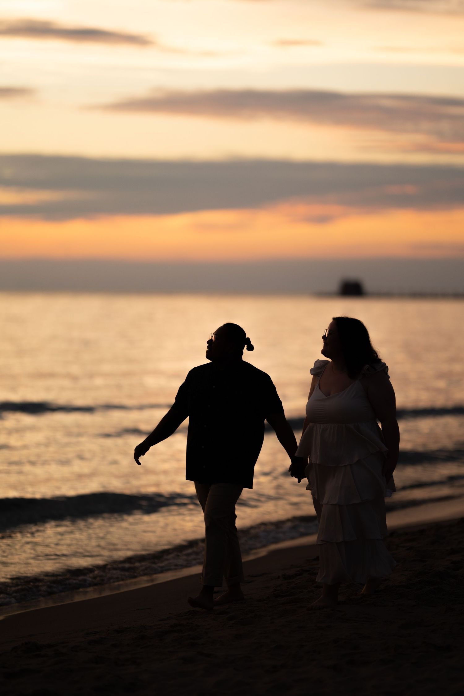 Romantic couple silhouette holding hands walking on beach at colorful sunset with ocean backdrop.