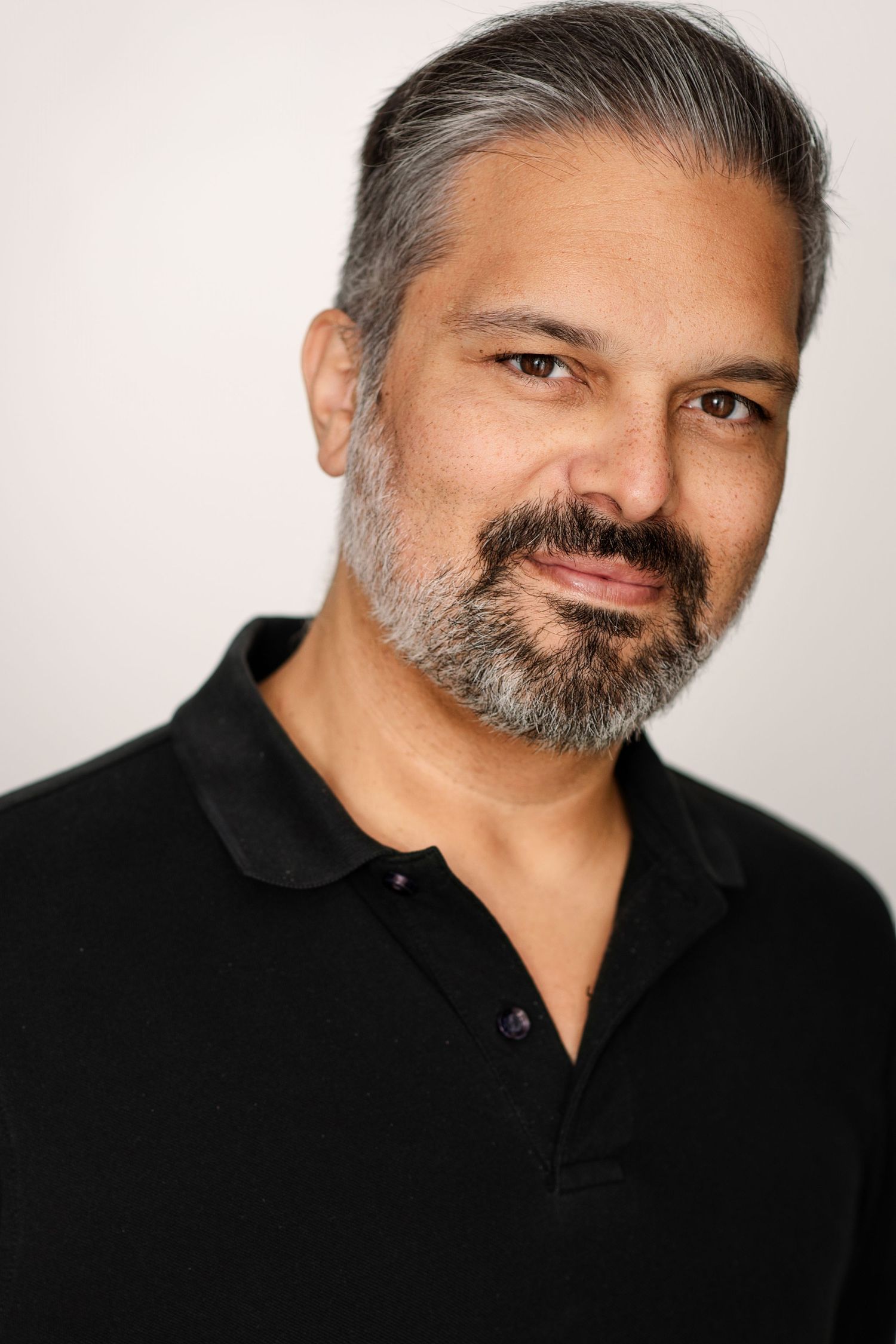 Headshot of a man with swept-back gray hair and a salt-and-pepper beard wearing a black polo shirt with a slight smile.