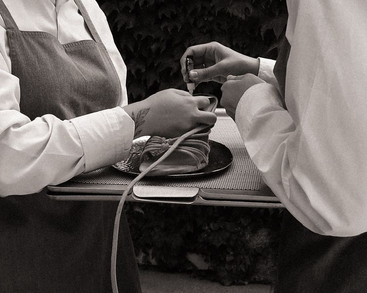 Black and white close-up of a waiter serving drinks on a tray at an outdoor wedding event.