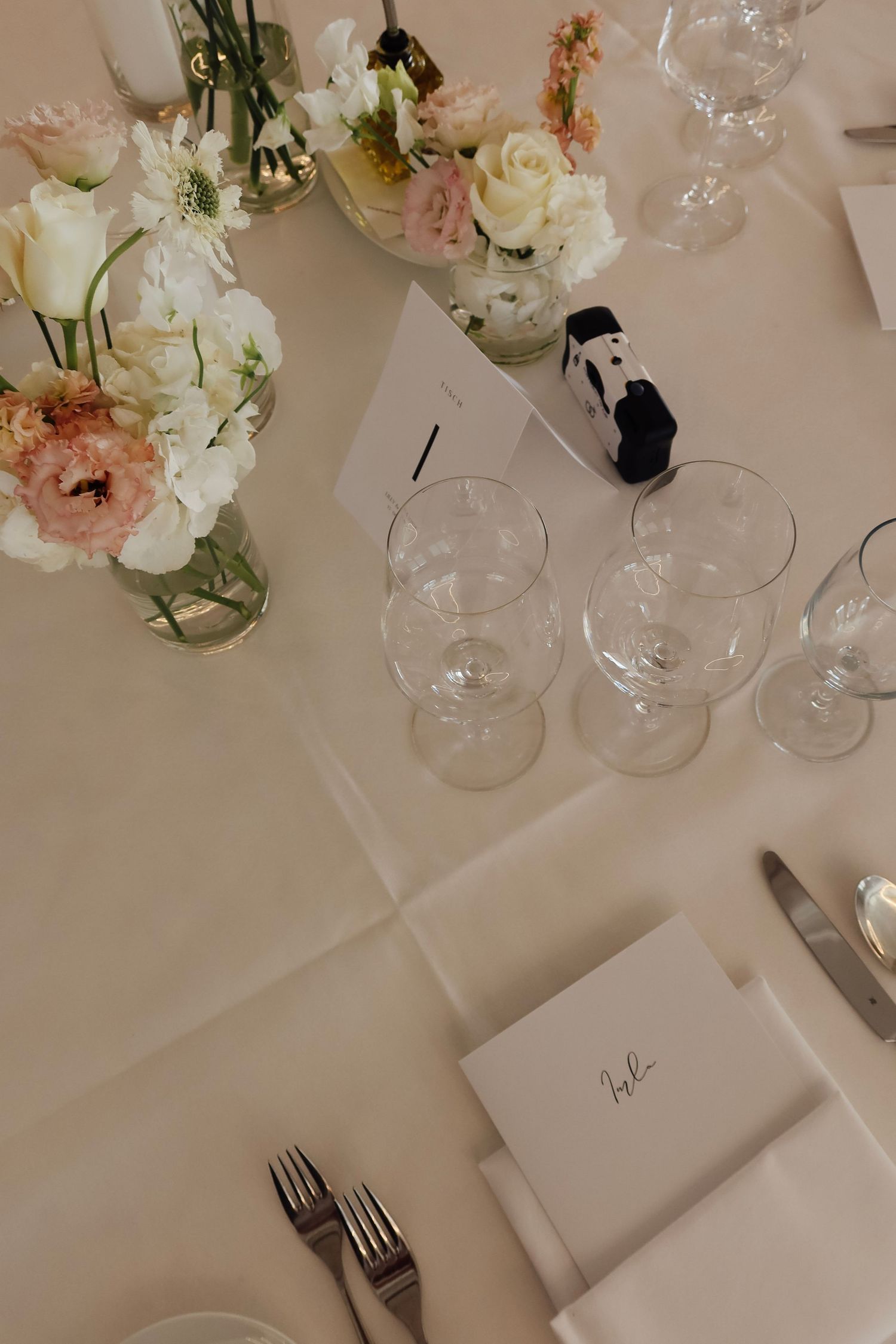 Elegant wedding reception table setting with pink and white floral arrangements, crystal glasses, and personalized menu cards.