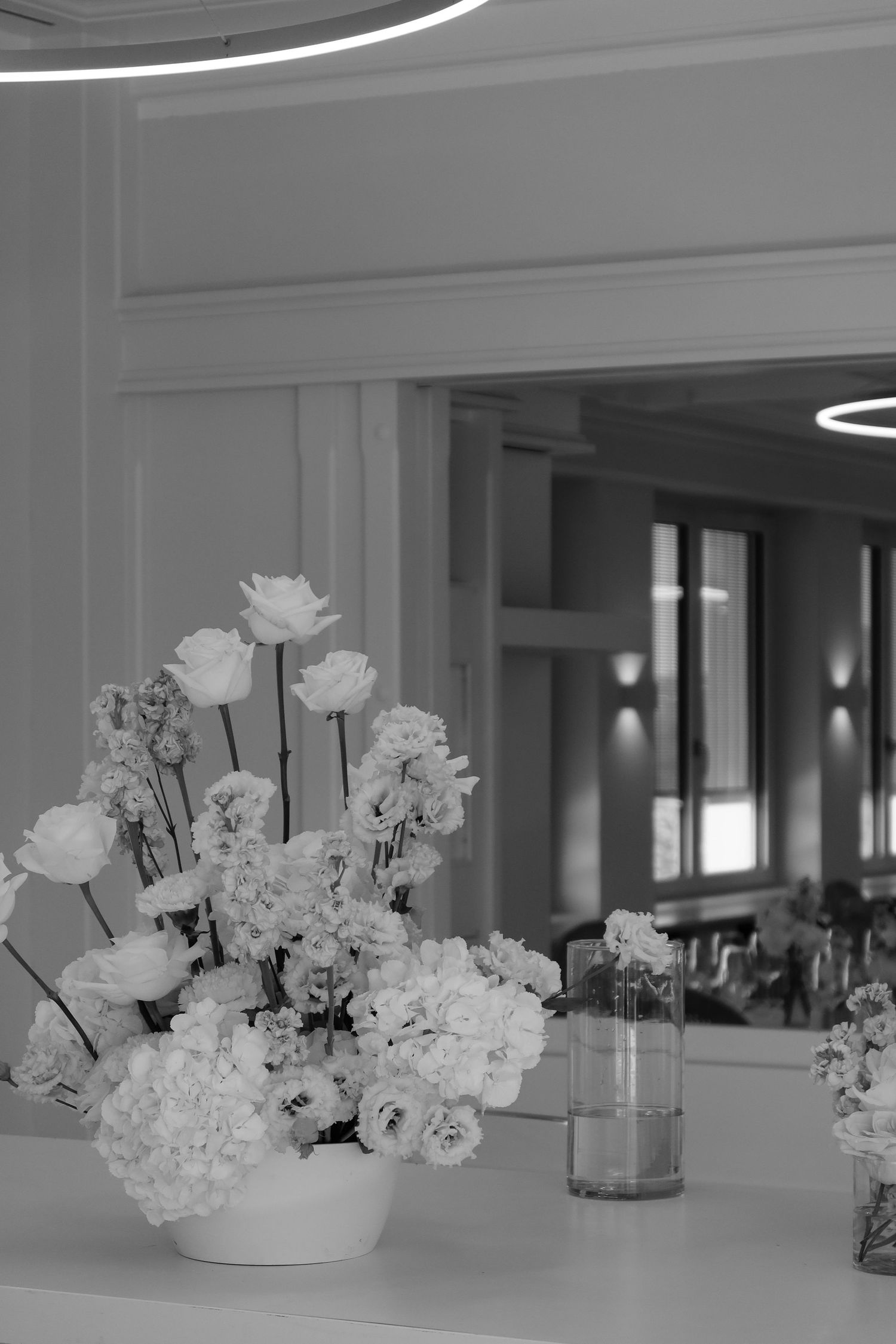 Elegant white floral centerpiece with roses in a vase on a reception table, black and white wedding photo.