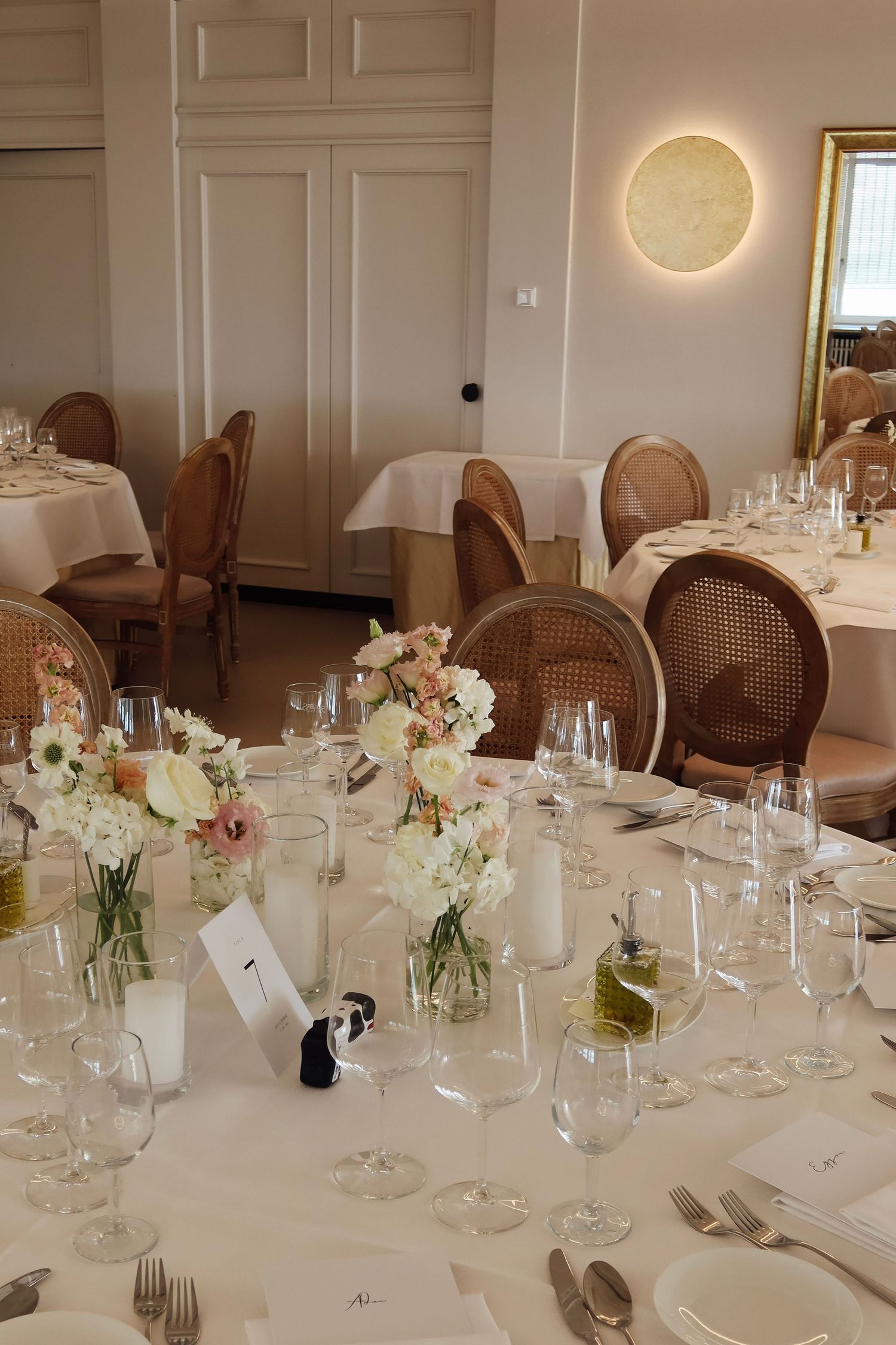 Elegant wedding reception table setting with white linens, crystal glasses, and blush floral centerpieces in a warm venue.