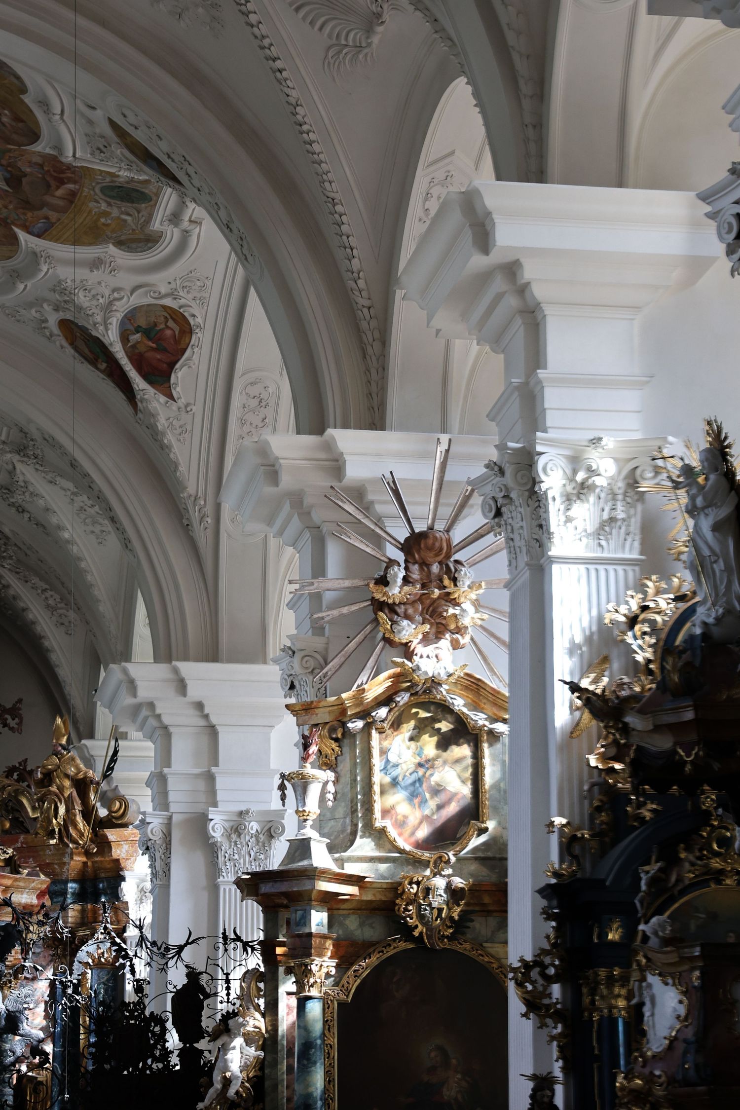 Ornate baroque church interior with gilded pulpit, white arched columns, and painted ceiling frescoes.