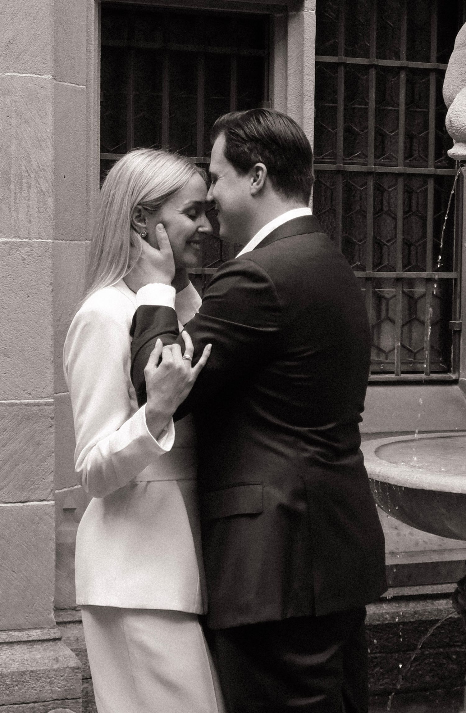 Black and white intimate photo of groom tenderly cupping brides face near stone fountain.