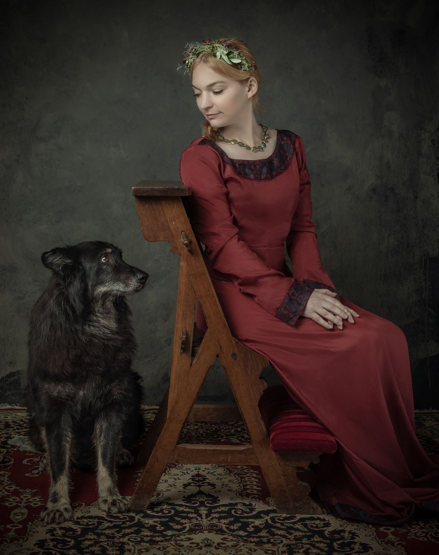 Elegant woman in red medieval gown sits on wooden chair beside black dog on ornate carpet.