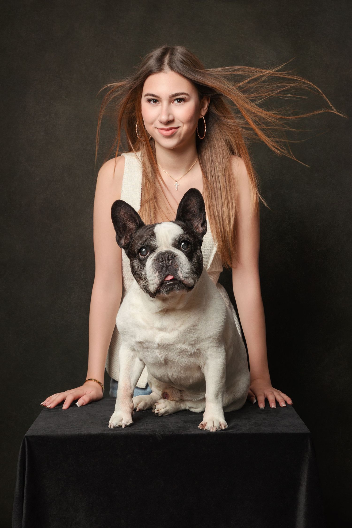 Young woman with flowing hair poses with a black and white French Bulldog on a dark studio background.