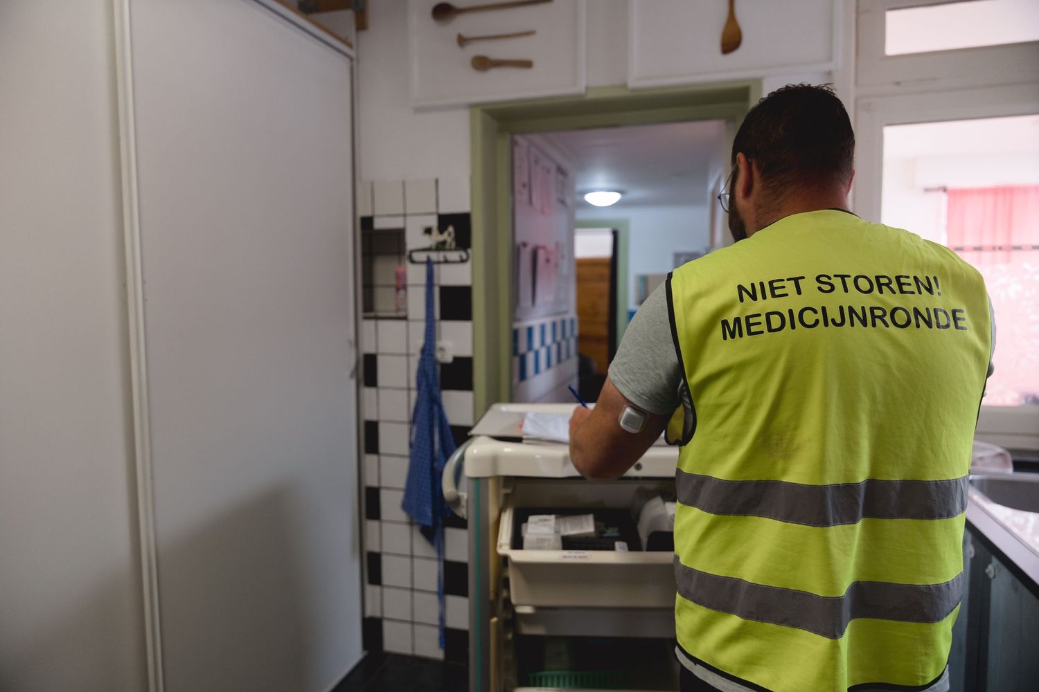 Worker in yellow safety vest labeled Niet Storen Medicijnronde preparing medication in a facility.