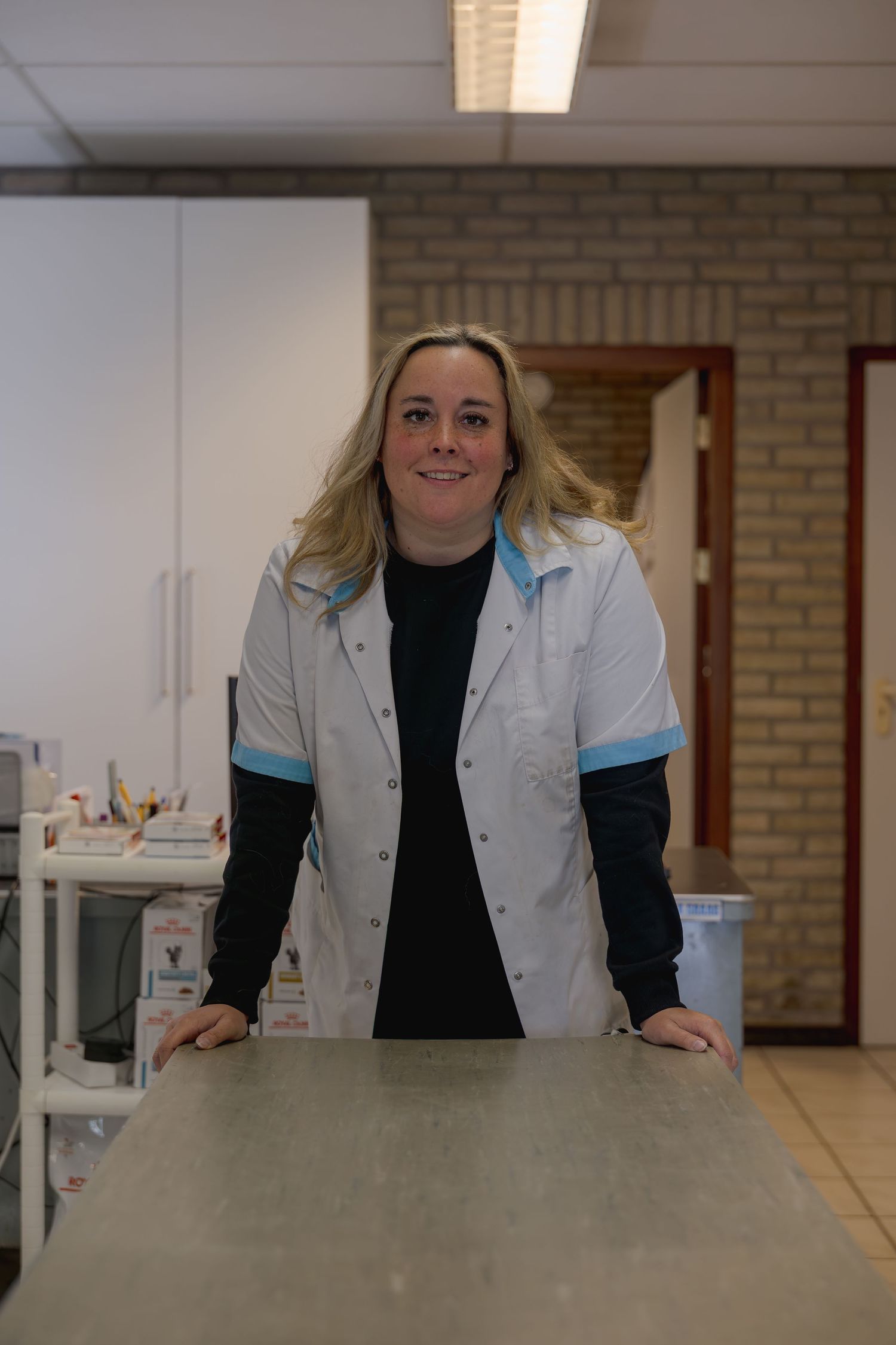 Smiling female veterinarian in white lab coat leaning on an examination table in a clinic.