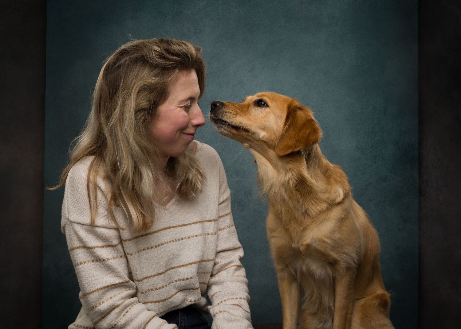 A woman in a cream sweater smiles warmly at a golden retriever during a professional studio portrait session.