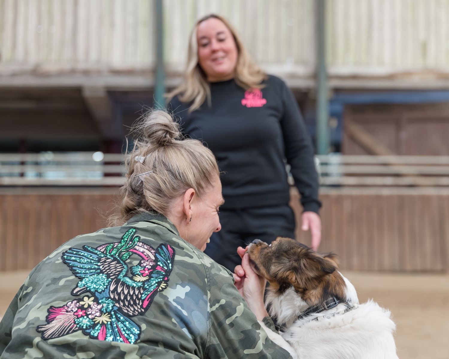 Woman in camo jacket cuddling a small dog during a training session indoors.