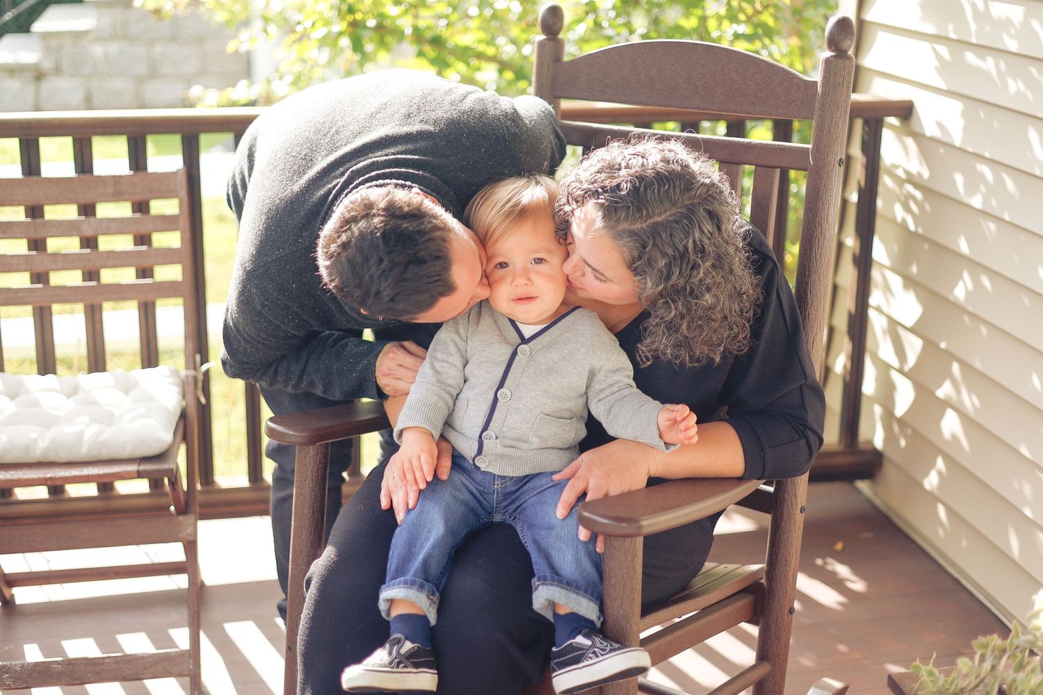 Parents kissing their baby on a porch swing during a New Jersey family portrait session