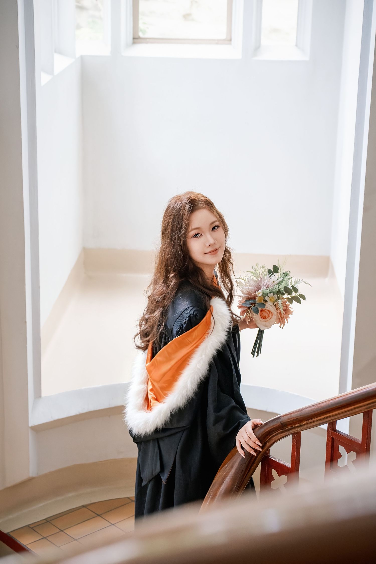 Indoor graduation photography portrait of a beautiful student holding flowers on a wooden staircase in Auckland. uoa Clock tower