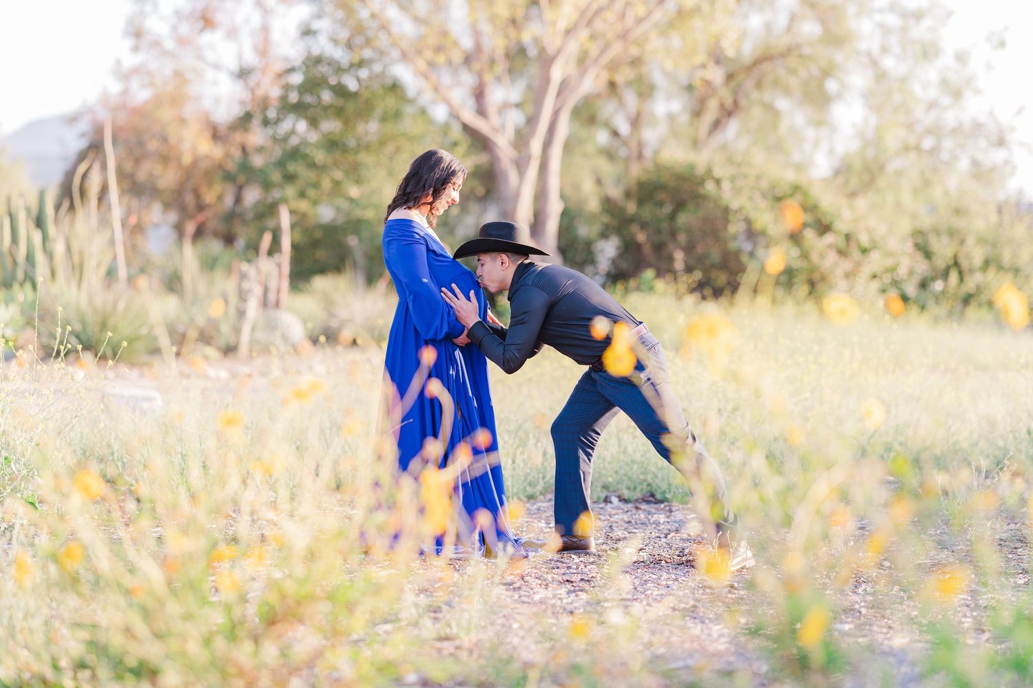 A couple in blue and black outfits takes engagement photos in a golden autumn field at sunset.