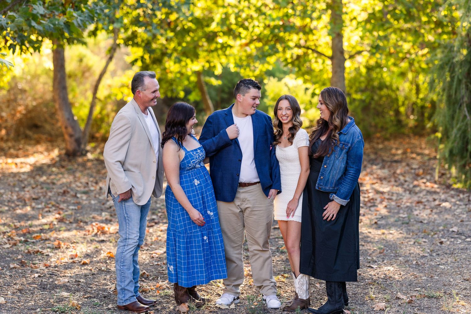 A family group enjoying candid moments together while walking through golden autumn leaves in a park setting.