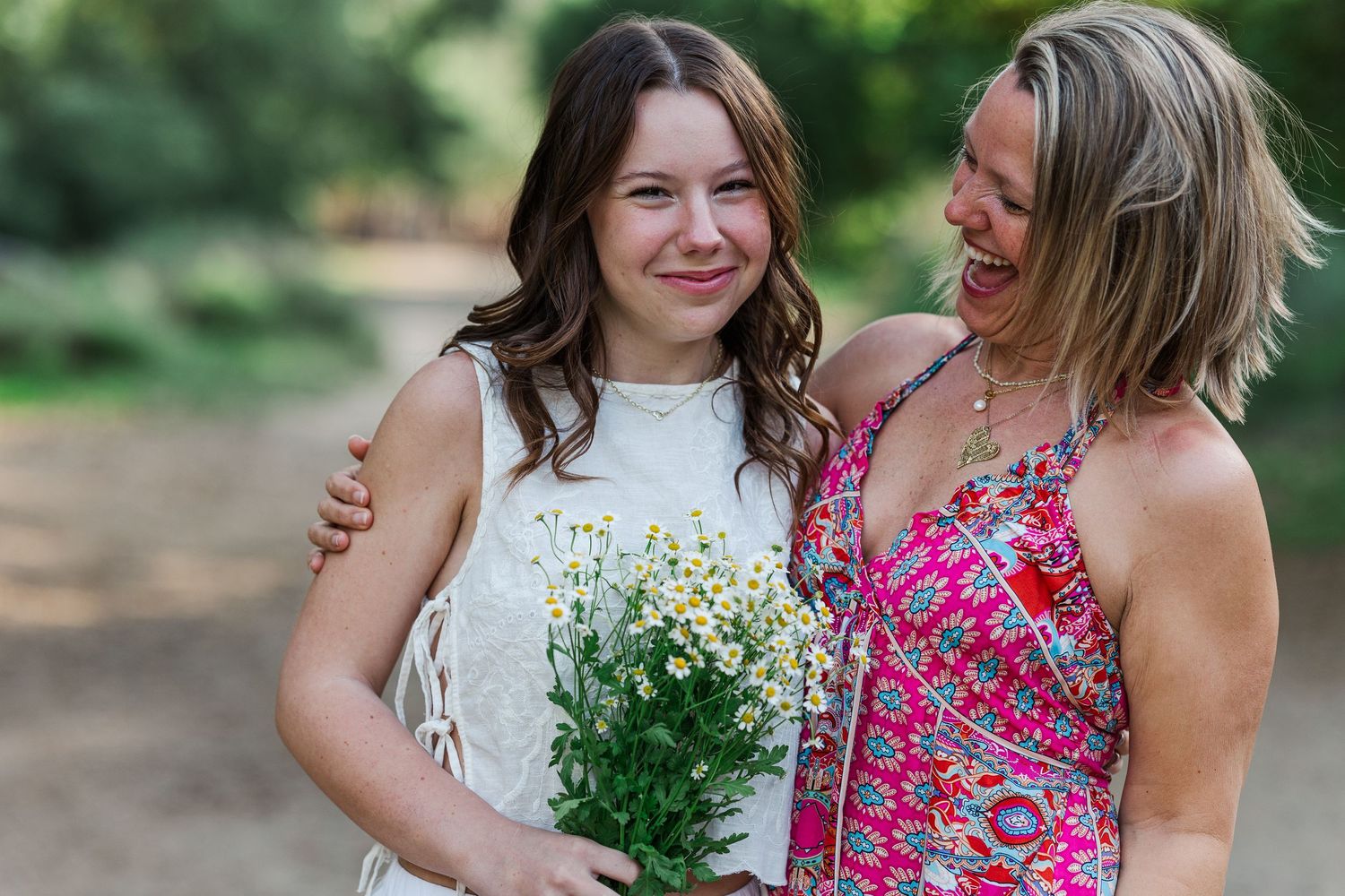 Mother and daughter walking hand in hand through a garden wearing coordinating white and pink floral dresses.