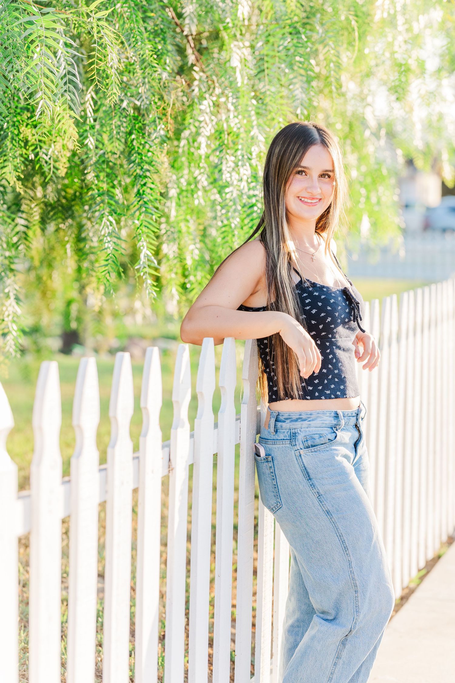 A series of outdoor portrait photos showing someone in a polka dot top and jeans posing by a white picket fence.