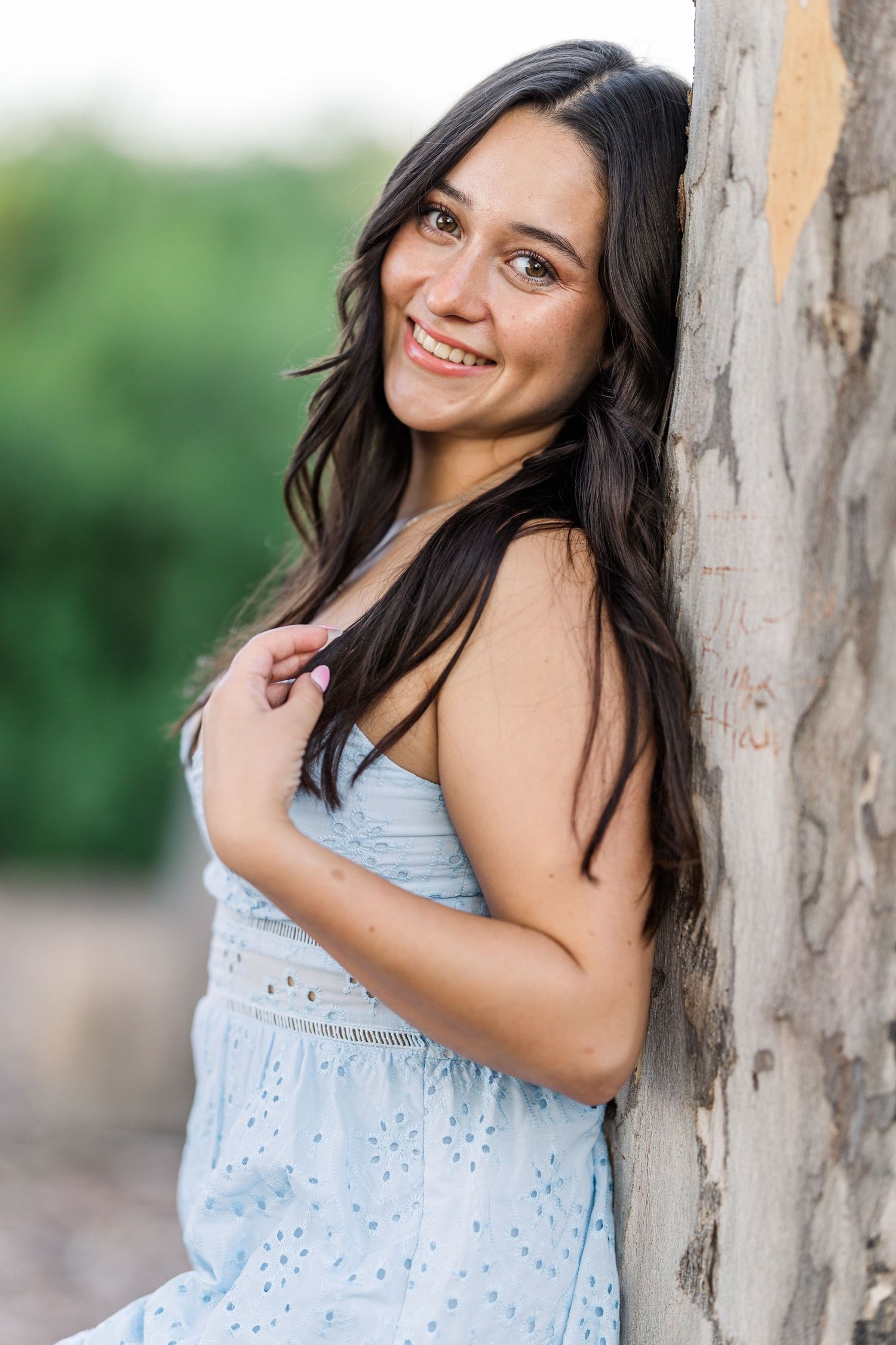 A series of outdoor portrait photos showing someone in a light blue summer dress posing against a tree trunk.