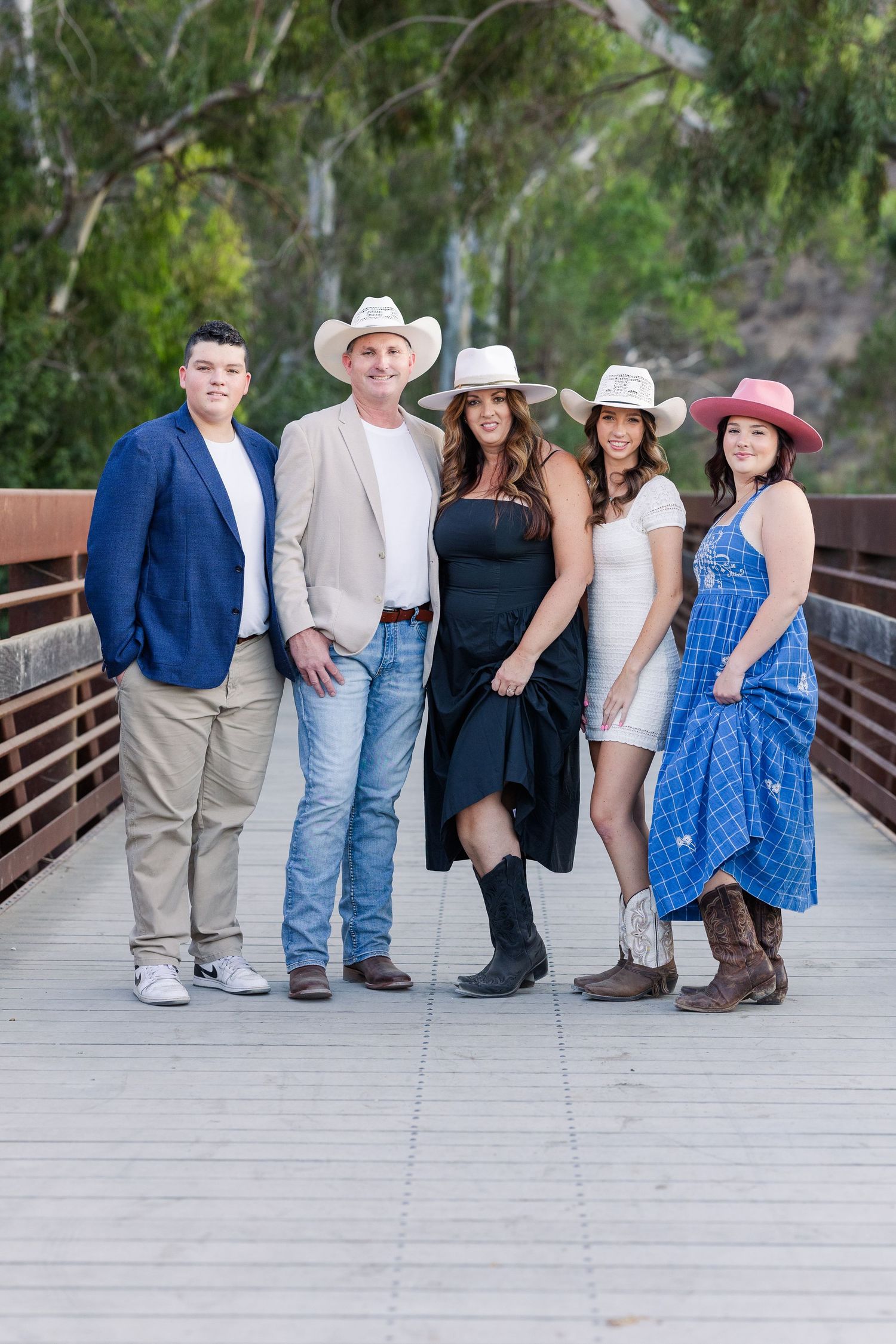 A group of five people in western attire pose together on a wooden bridge surrounded by lush greenery.