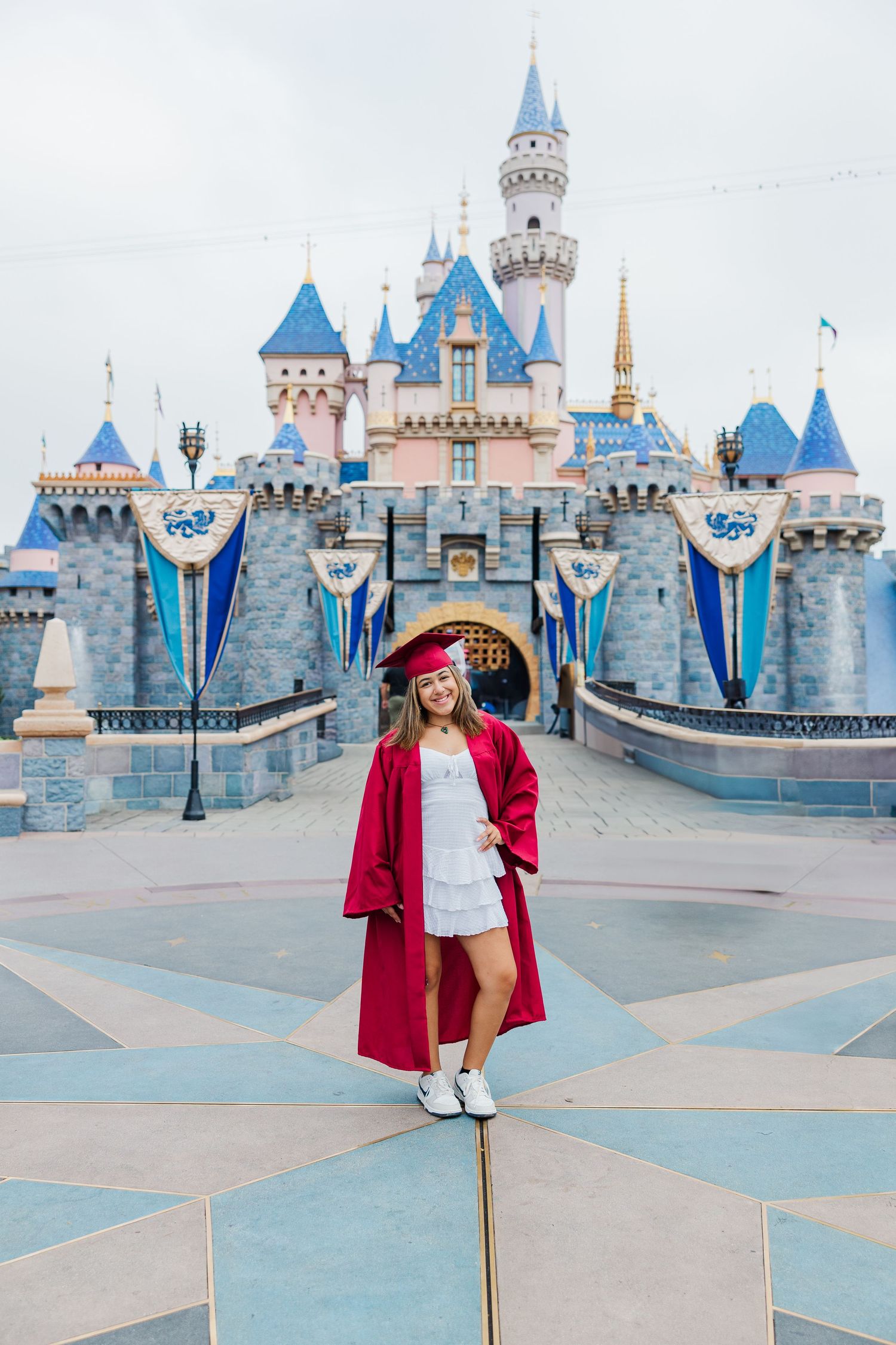 A visitor poses in front of Disneyland's iconic Sleeping Beauty Castle on a cloudy morning.