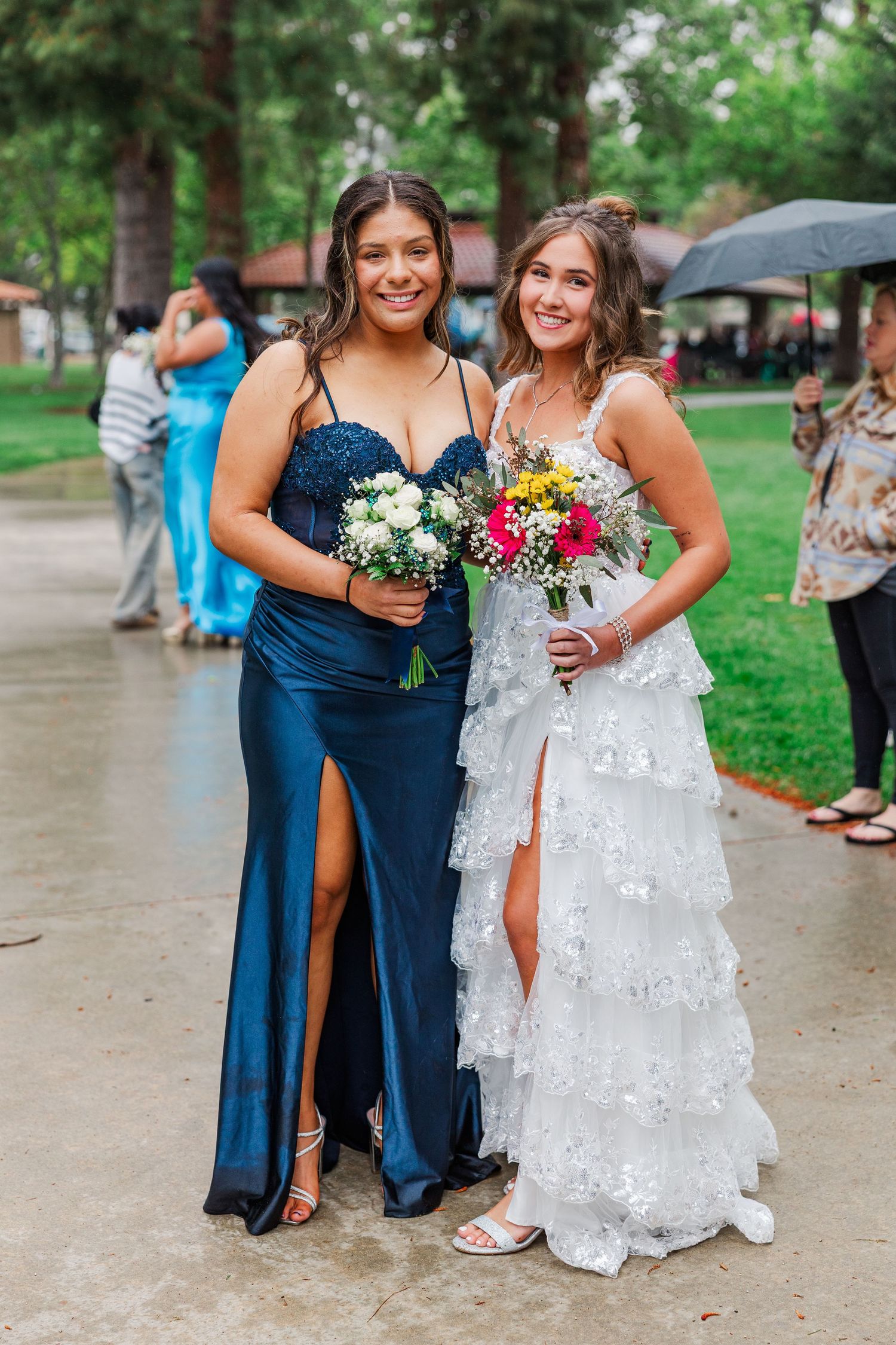 A wedding party poses together on a rainy day, with bridesmaids in navy blue dresses and a bride in white lace gown.