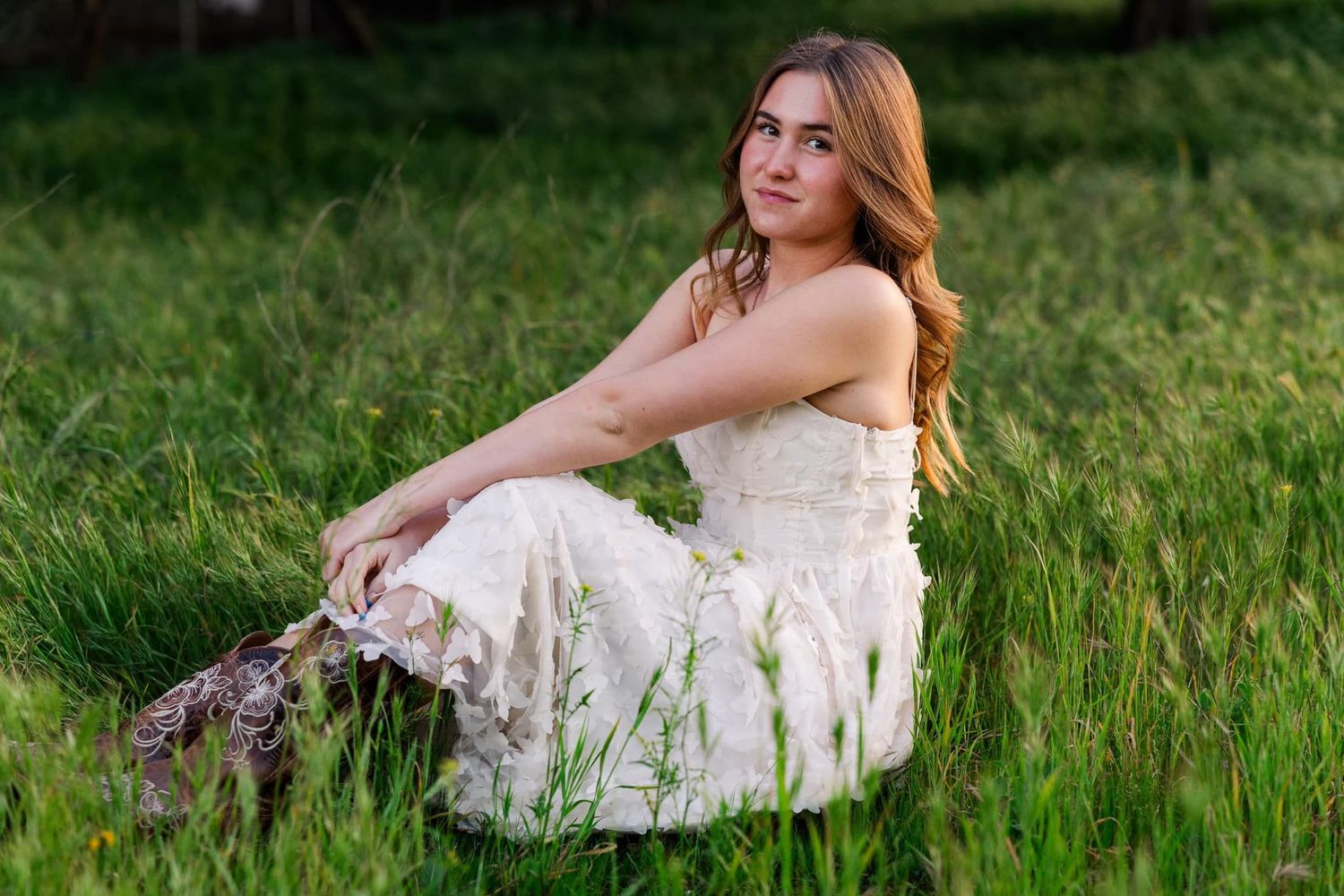 A person wearing a white lace dress sits elegantly in a lush green meadow during a warm summer day.