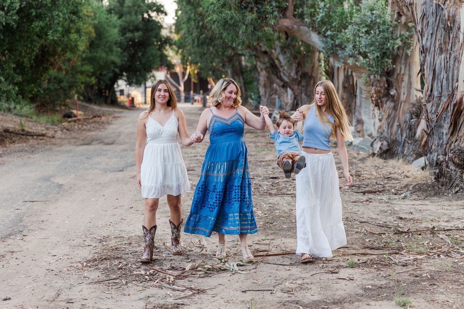 A group dressed in coordinating blue and white outfits stands together near tall eucalyptus trees during an outdoor photo shoot.