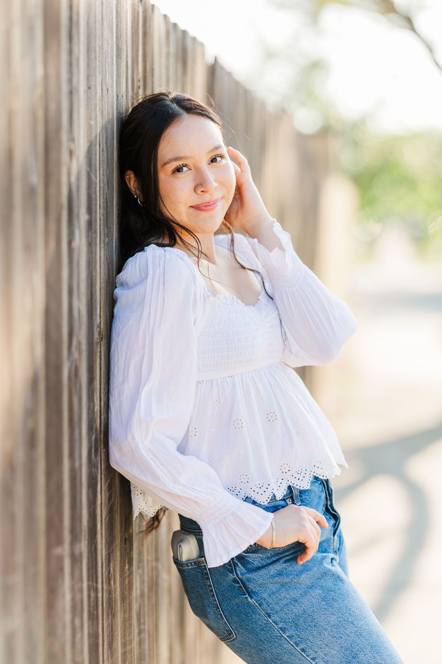 A person in a white blouse and jeans poses against a wooden fence in a series of casual outdoor portraits.