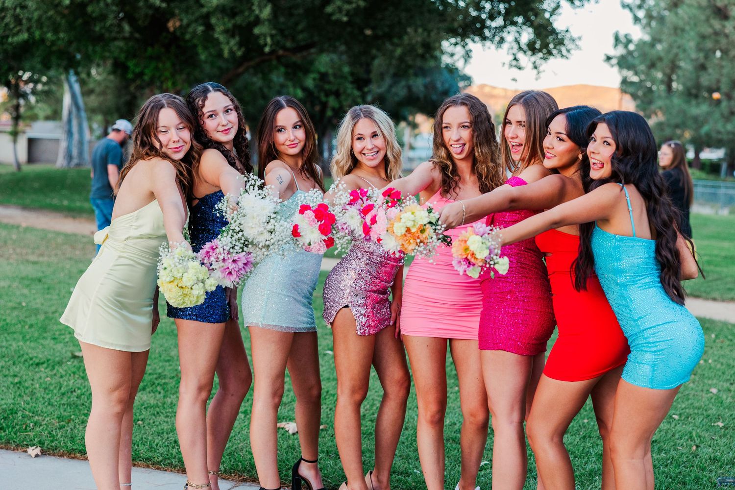 A line of people wearing colorful swimsuits and summer clothing pose together outdoors on grass.