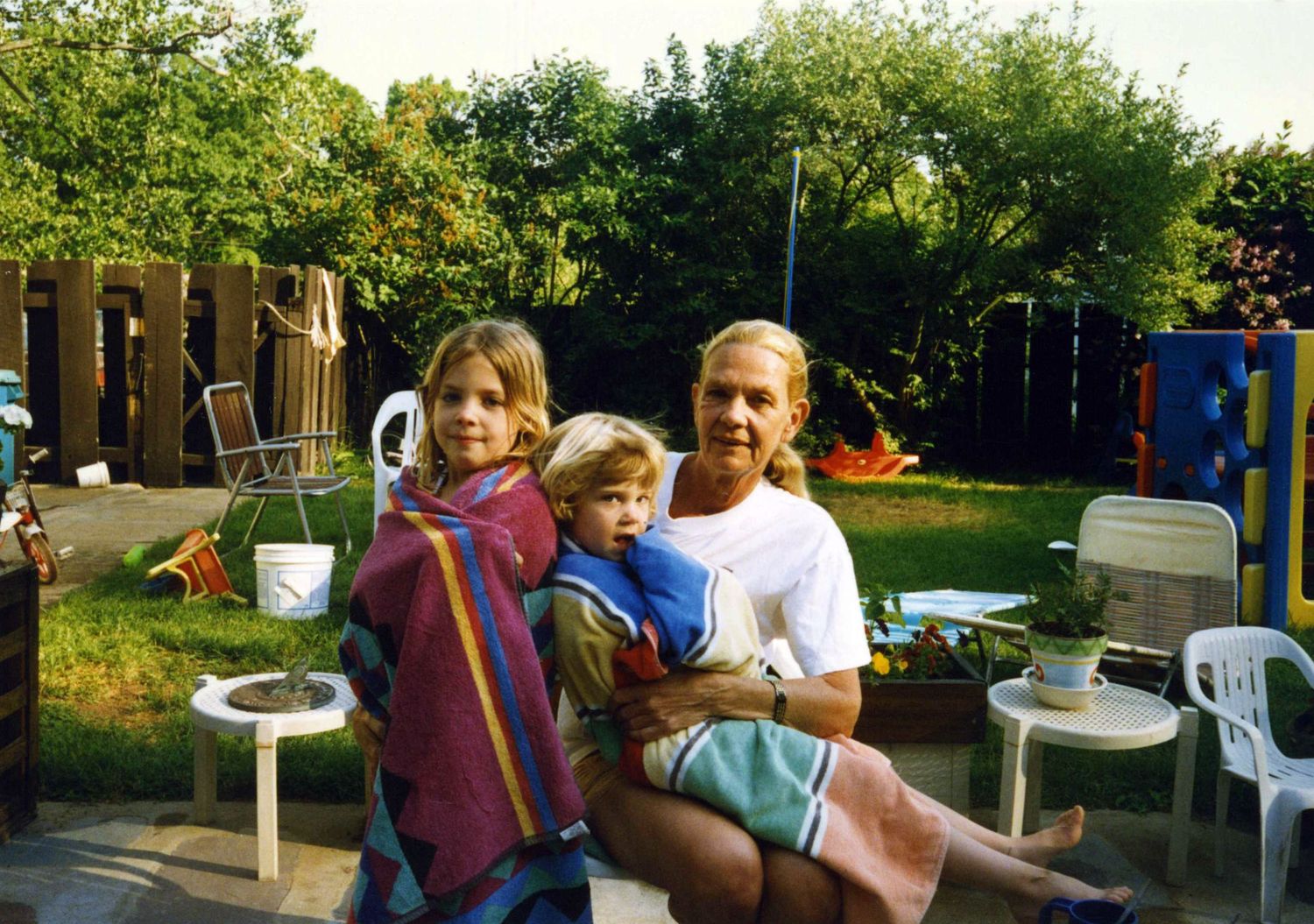 Vintage photo of family gathering in backyard with plastic chairs and playground equipment.