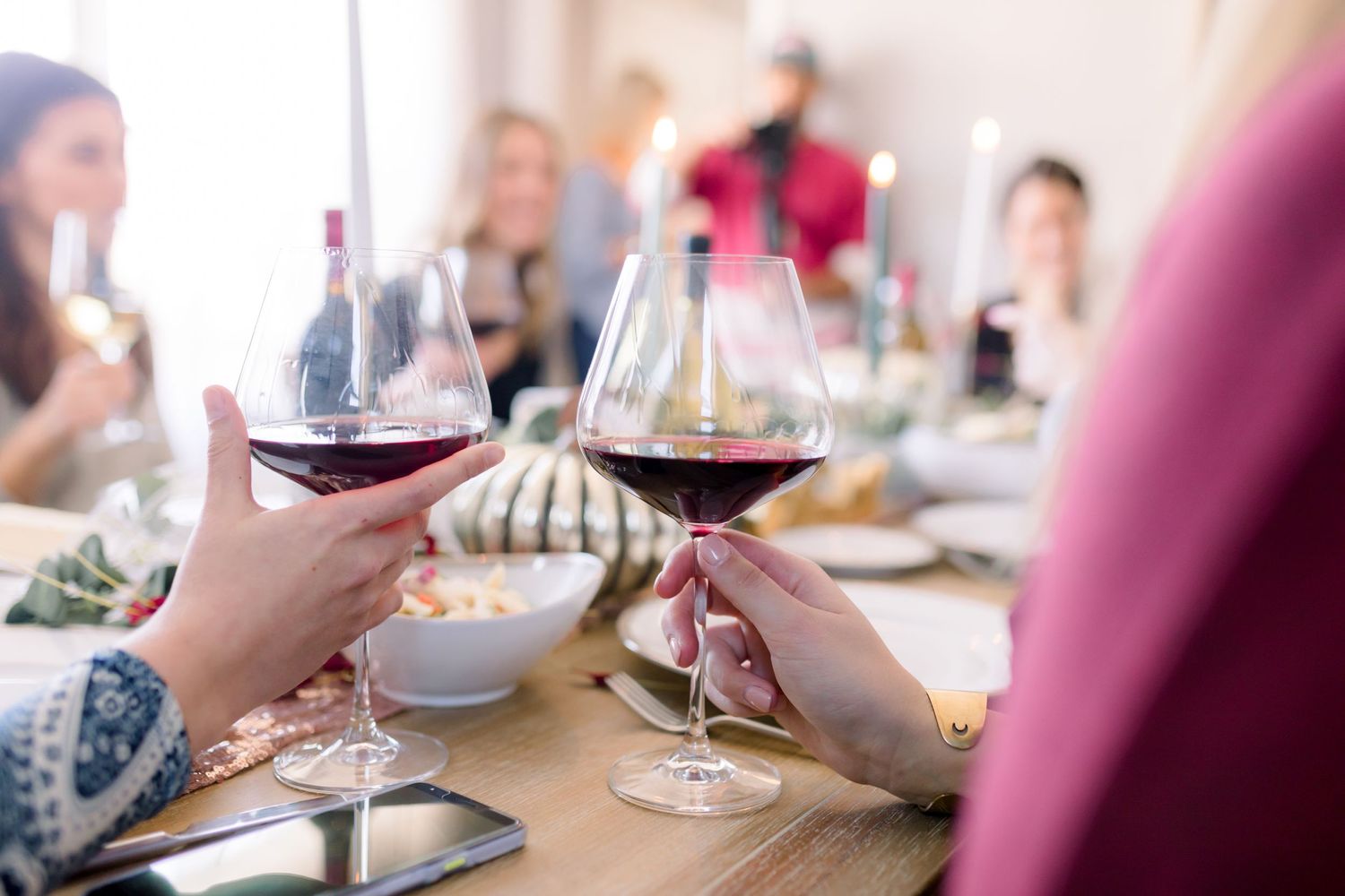Friends toasting with red wine glasses over a dinner table.