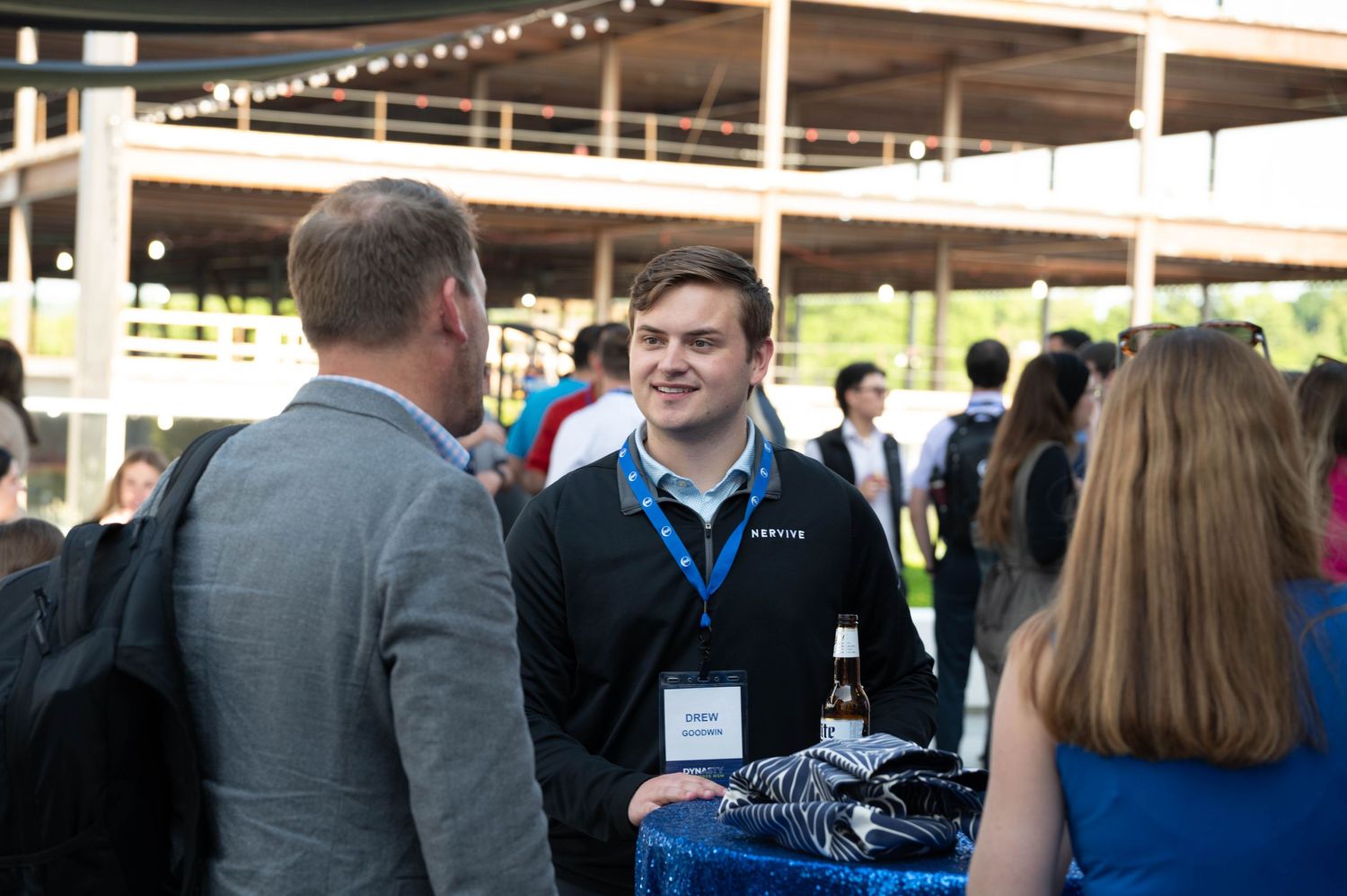 People mingling at an outdoor networking event under string lights with beverages and casual conversation.