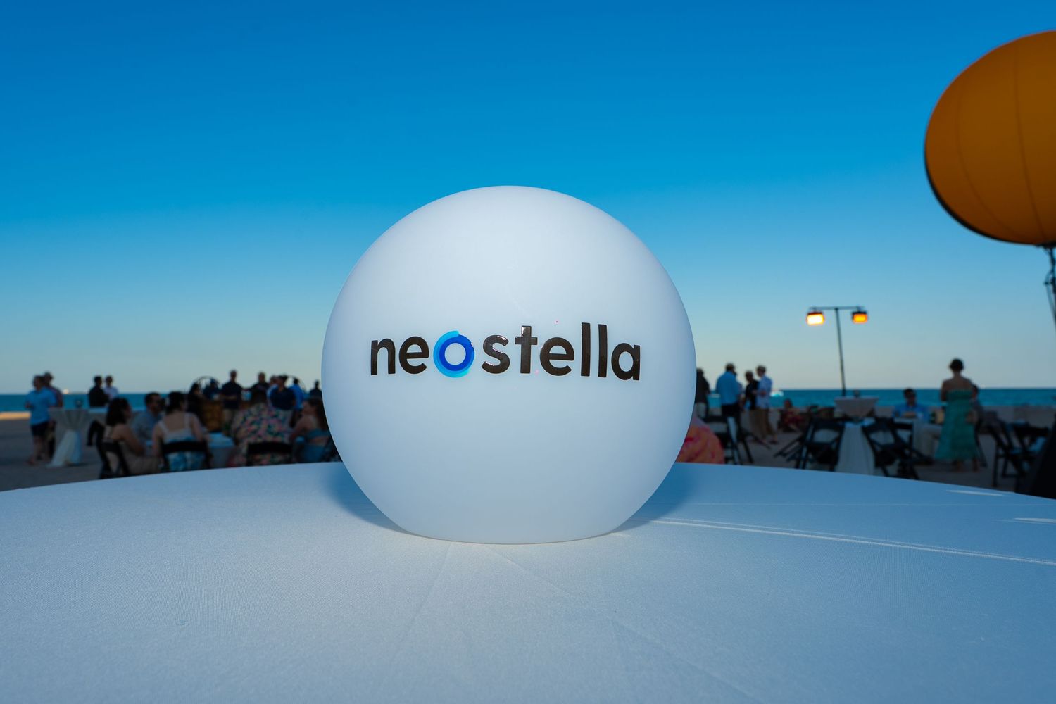 Large white inflatable sphere with Neostella logo displayed outdoors near a beachfront at dusk.
