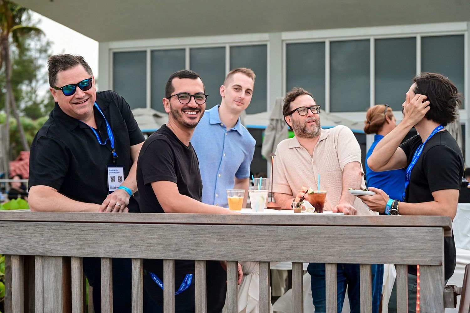 Group of five professionals socializing outdoors at a high-top table with drinks at a networking event.