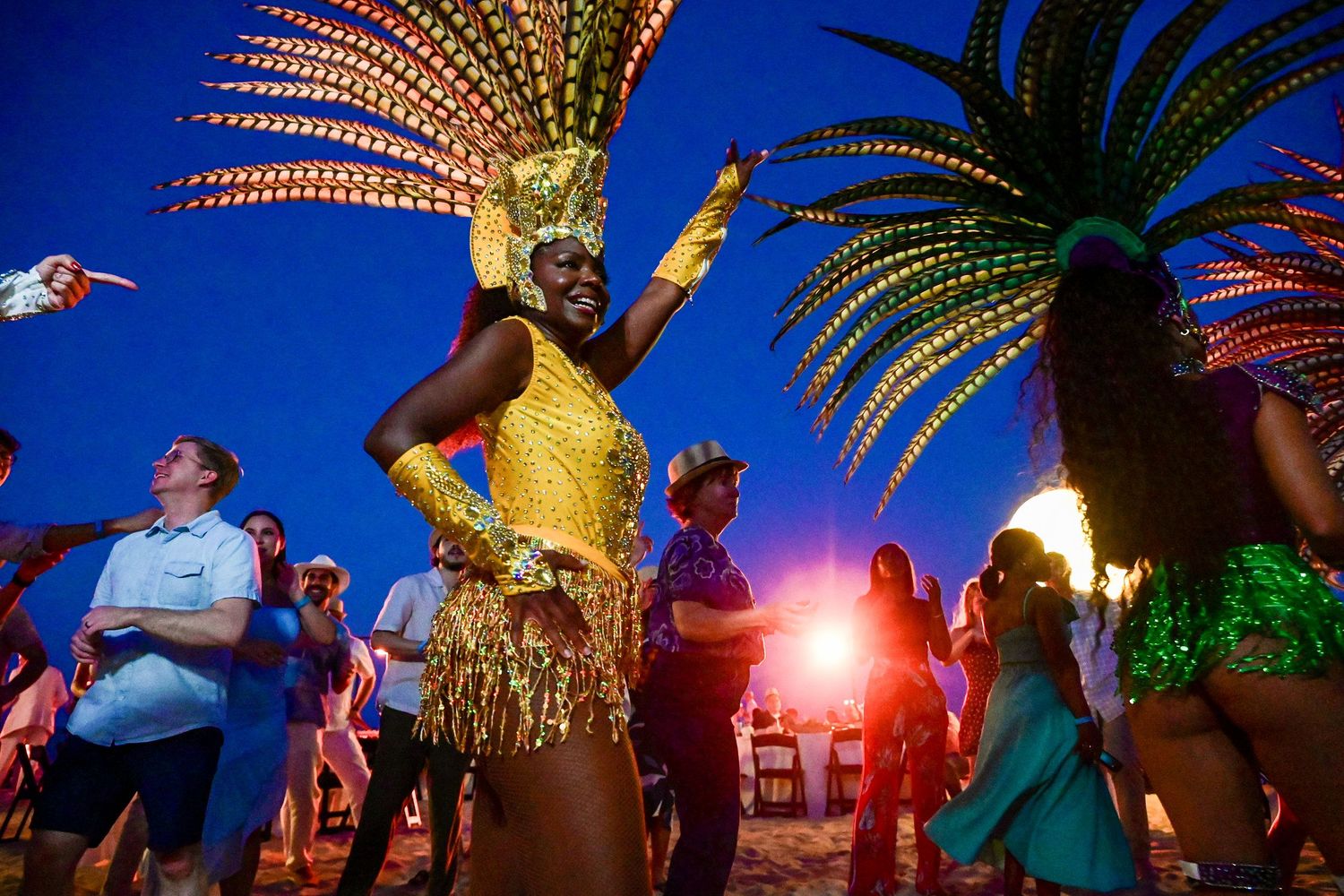 Vibrant carnival dancer in gold costume with feathered headdress performs at a twilight beach festival.